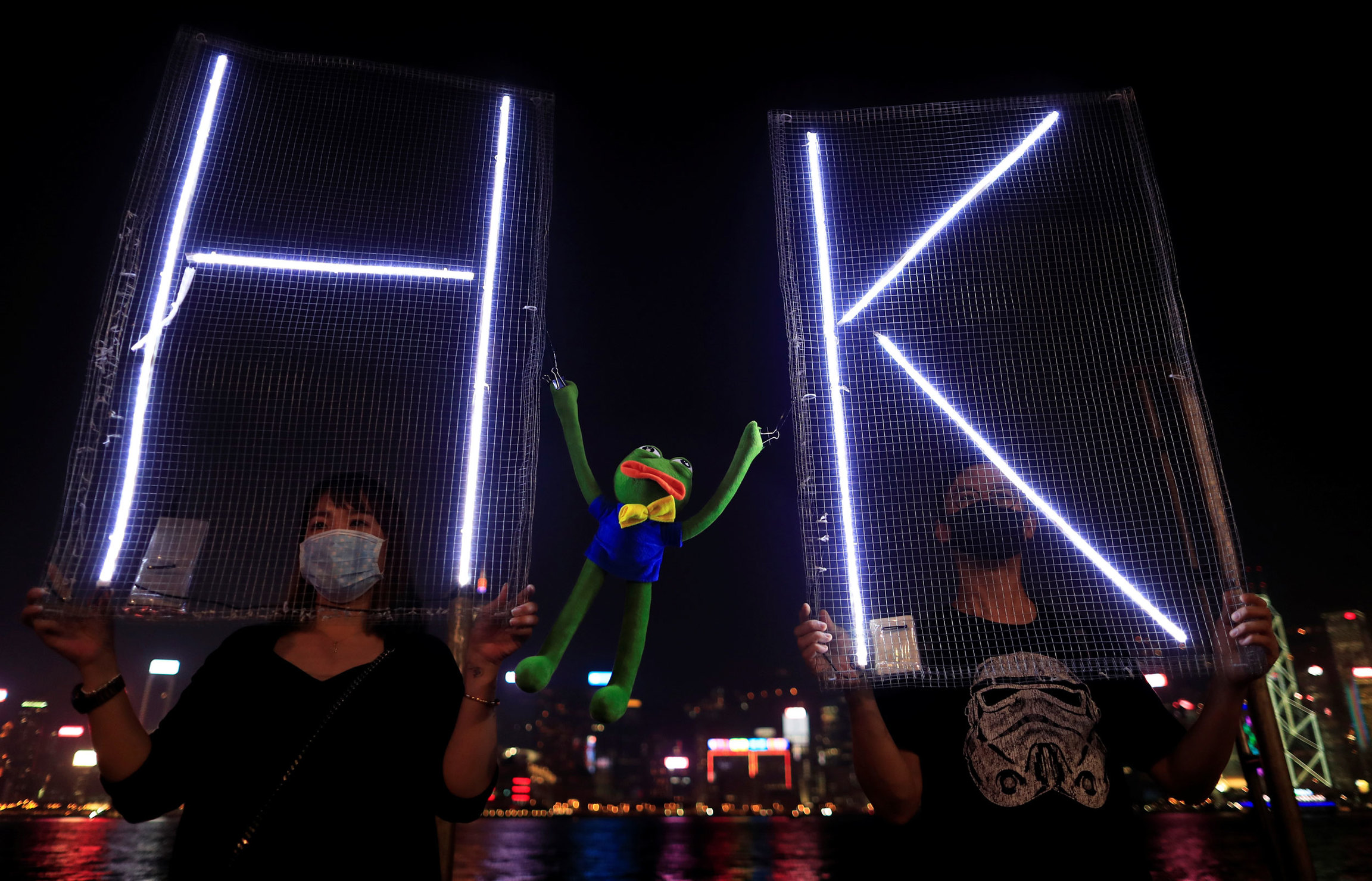 Anti-government protesters hold a Pepe the Frog plush toy, which has become a symbol of resistance for demonstrators in Hong Kong, Sept. 30, 2019. Two people are shown holding signs with electrified letters H and K with a Pepe the Frog plush toy inbetween.