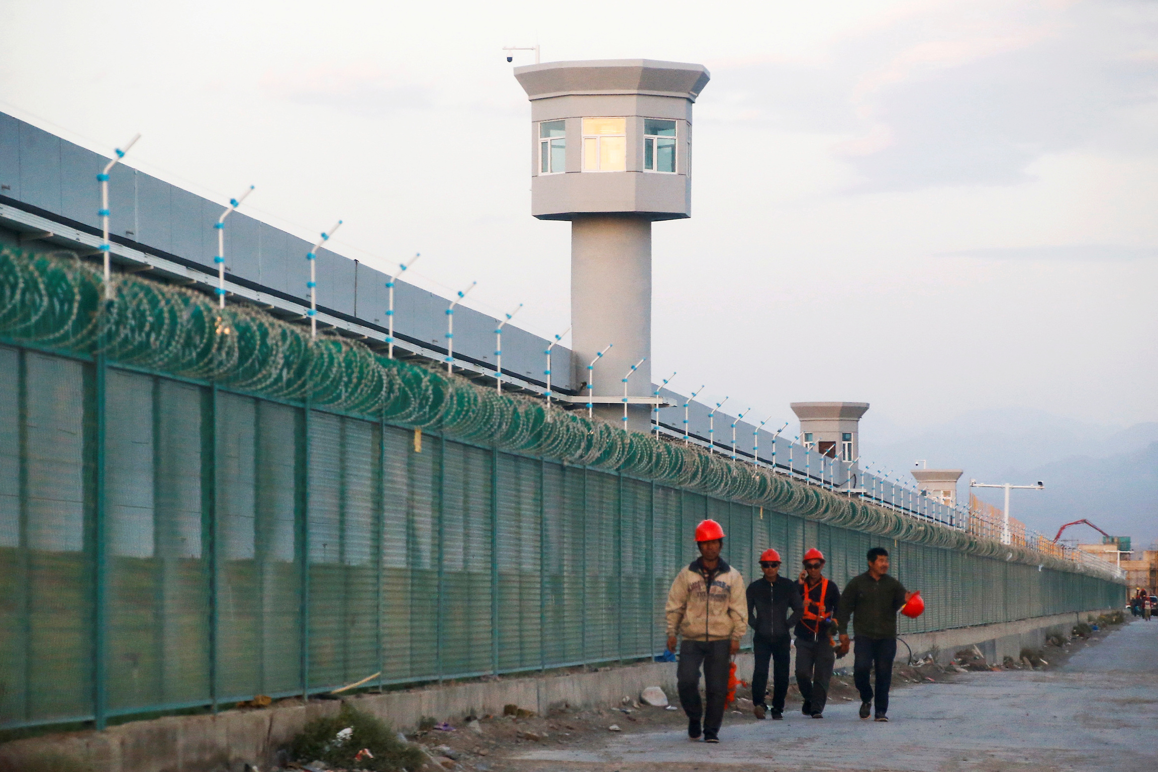 Four workers in uniform walk near a long, green fence.
