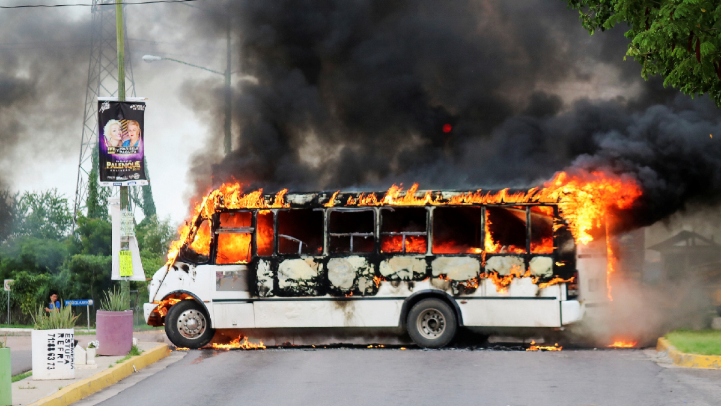 Bus set alight by cartel gunmen to block a road in Culiacan, Mexico. a white bus is engulfed in flames.