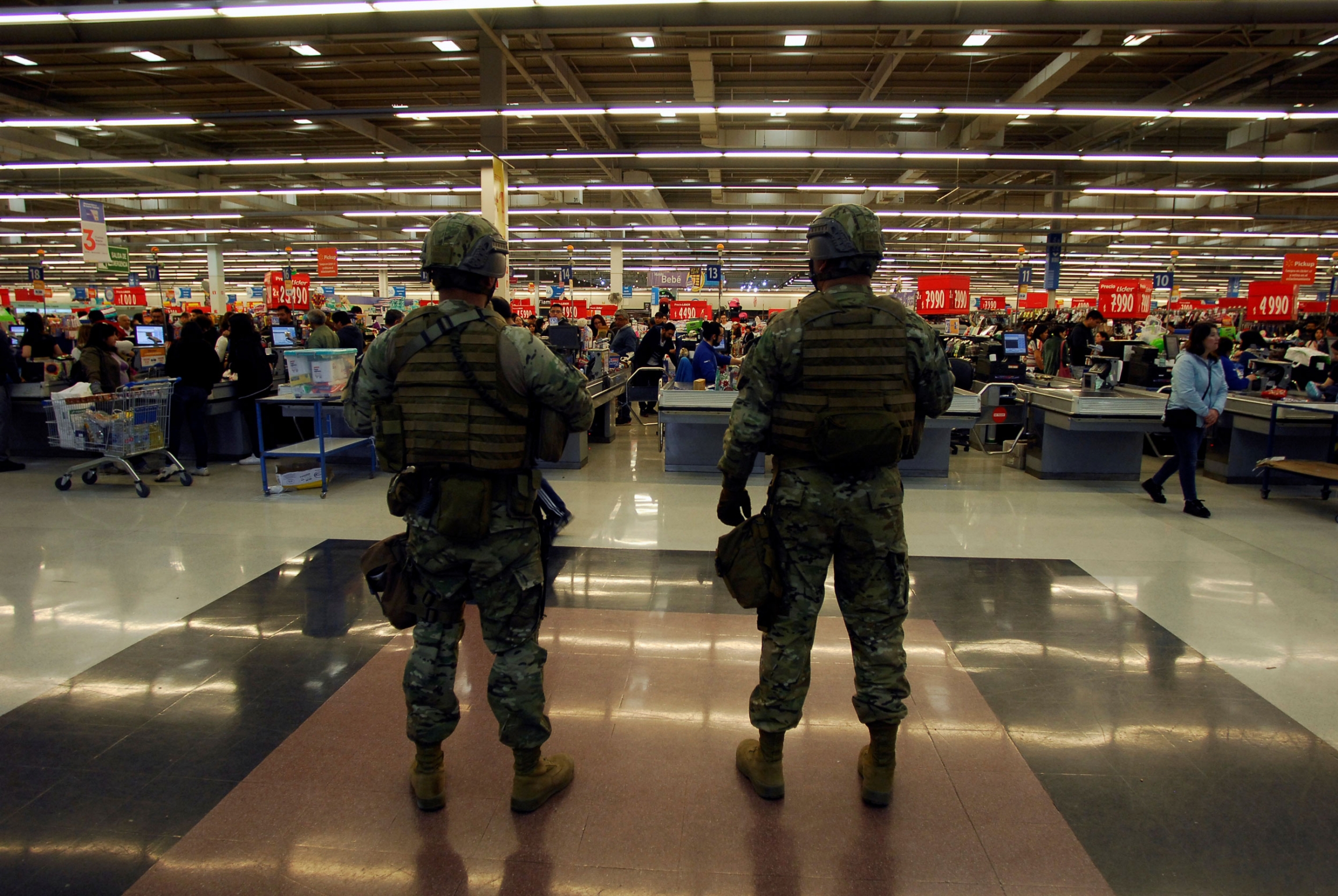 Soldiers stand guard inside a supermarket a day after a protests against the government, in Concepcion, Chile, Oct. 20, 2019. Soldiers are shown stand guard wearing full combat armor and helmets with supermarket checkout lines in the background.