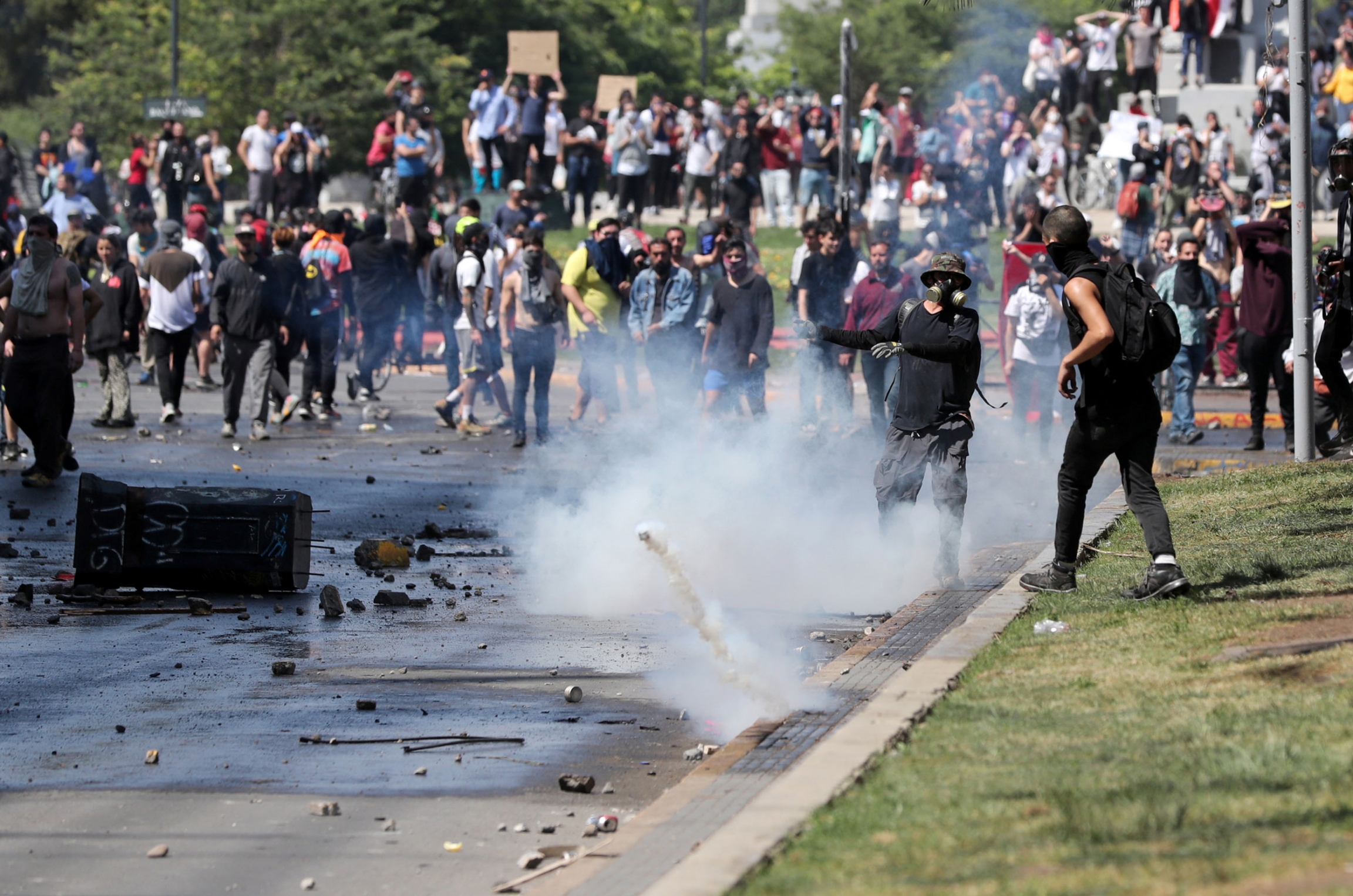 Demonstrators deflect a tear gas canister during a protest in Santiago, Chile, Oct. 20, 2019. A large group of protesters are shown in the street with a smoking tear gas canister bouncing through the middle of the group.