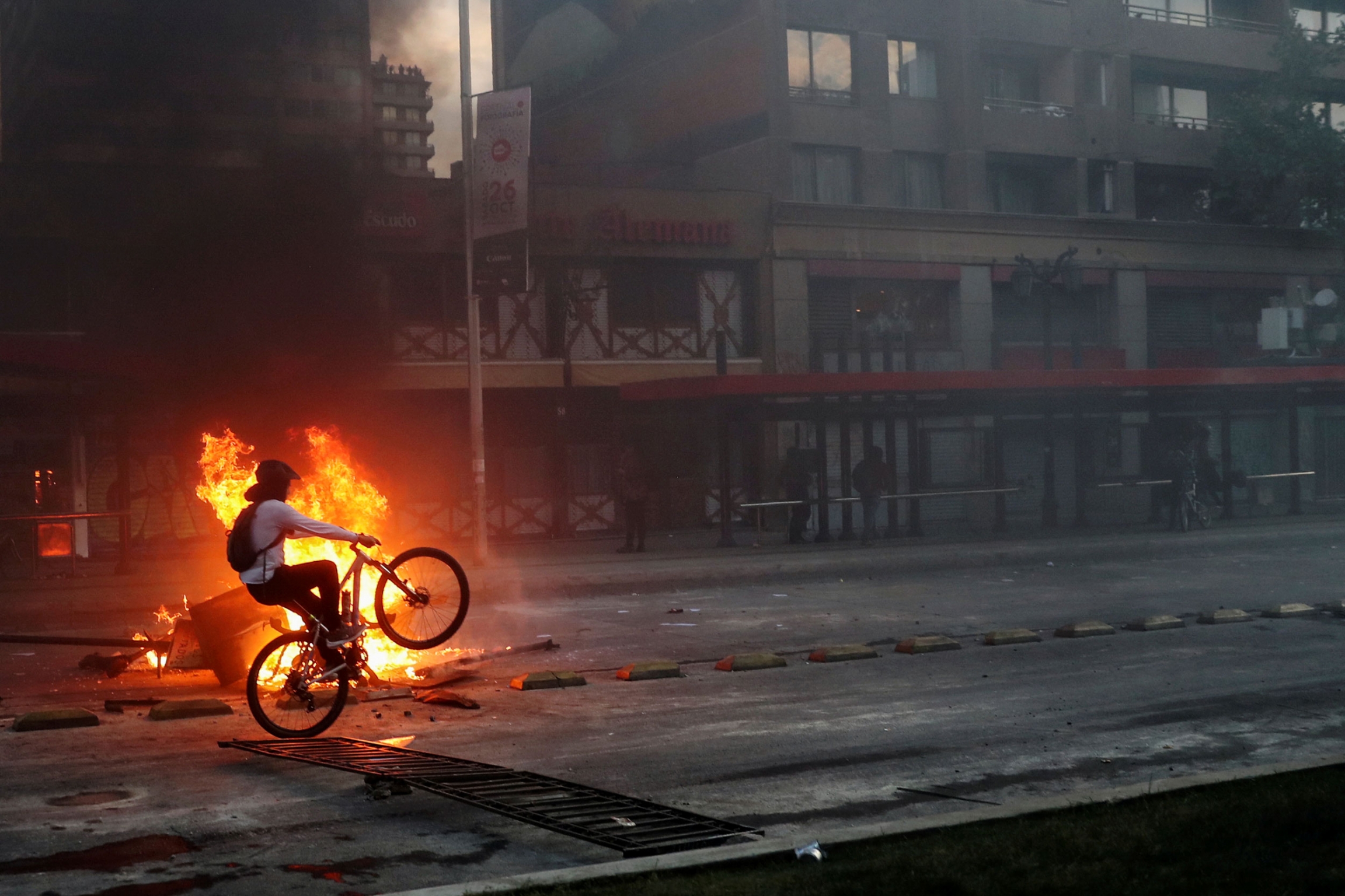 A demonstrator rides a bicycle past a bonfire during a protest in Santiago, Chile, Oct. 19, 2019. A demonstrator is shown on a bicycle riding a wheelie past a bright orange bonfire.