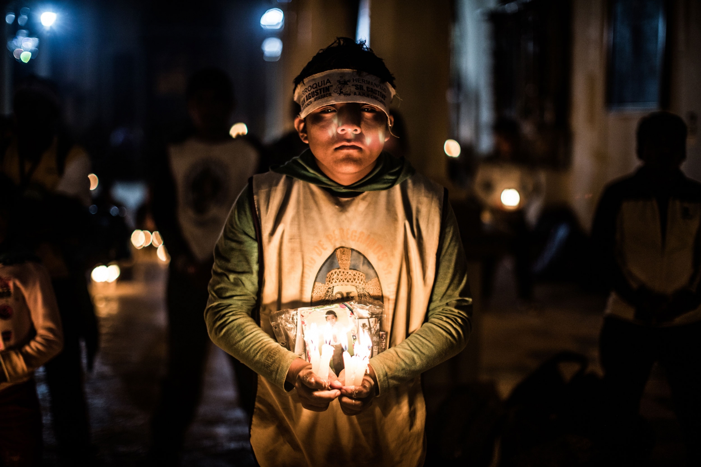 A pilgrim prays in the Temple of the Captive. Thousands of pilgrims walk days or months just to be able to look at and pray to the Captive. A you boy is shown holding several candles and a picture in a darkly lit photograph.