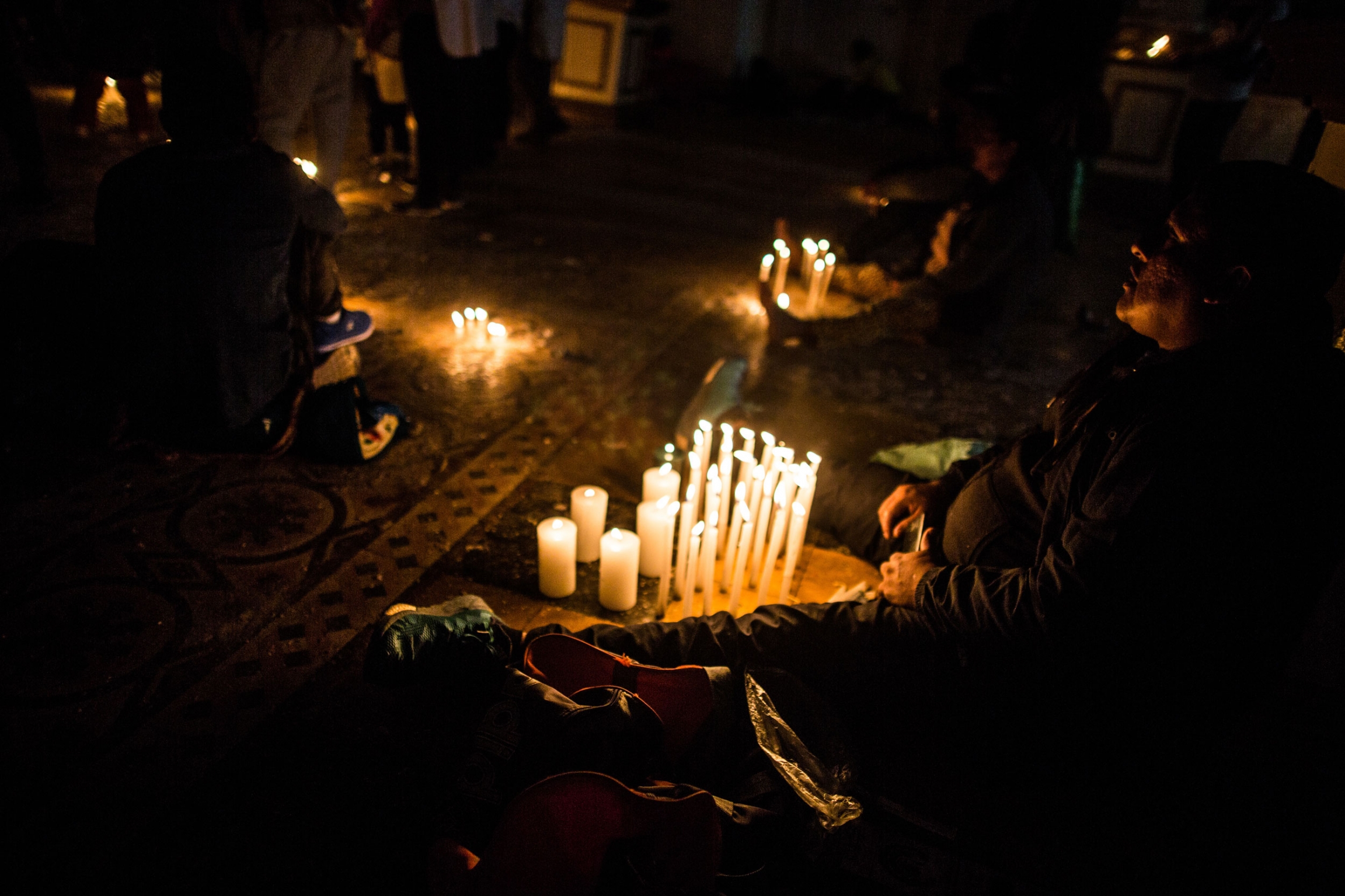Pilgrims light candles in the Temple of the Captive Lord to ask for a miracle for either themselves or a family member. Many miracles have been attributed to the Captive by believers — lame people who walk again, people who recover from drug addictions or A person is shown sitting on the ground with their legs on either side of a display of several lit candles.