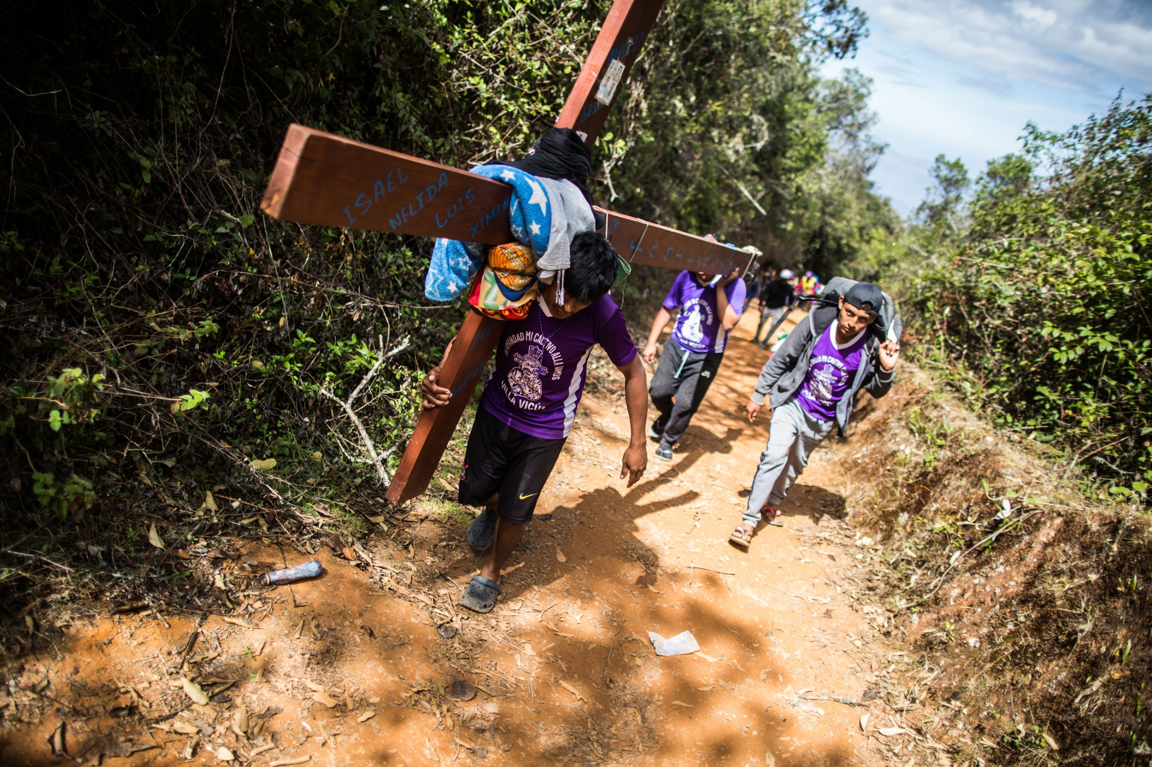 A pilgrim carries a cross in an area known as the “Devil's Nose.” It’s the last section before reaching Ayabaca. The crosses can weigh more than 200 pounds. A pilgrim is shown carrying a large cross and walking up a hill via a dirt path.