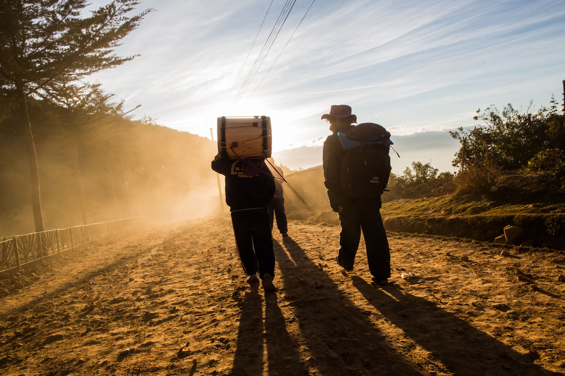 Some pilgrims bring musical instruments, and their songs can be heard along the journey to the Land of Captive. These groups of pilgrims are called "brotherhoods." A person is shown walking toward a setting sun and carrying a large drum on their back.