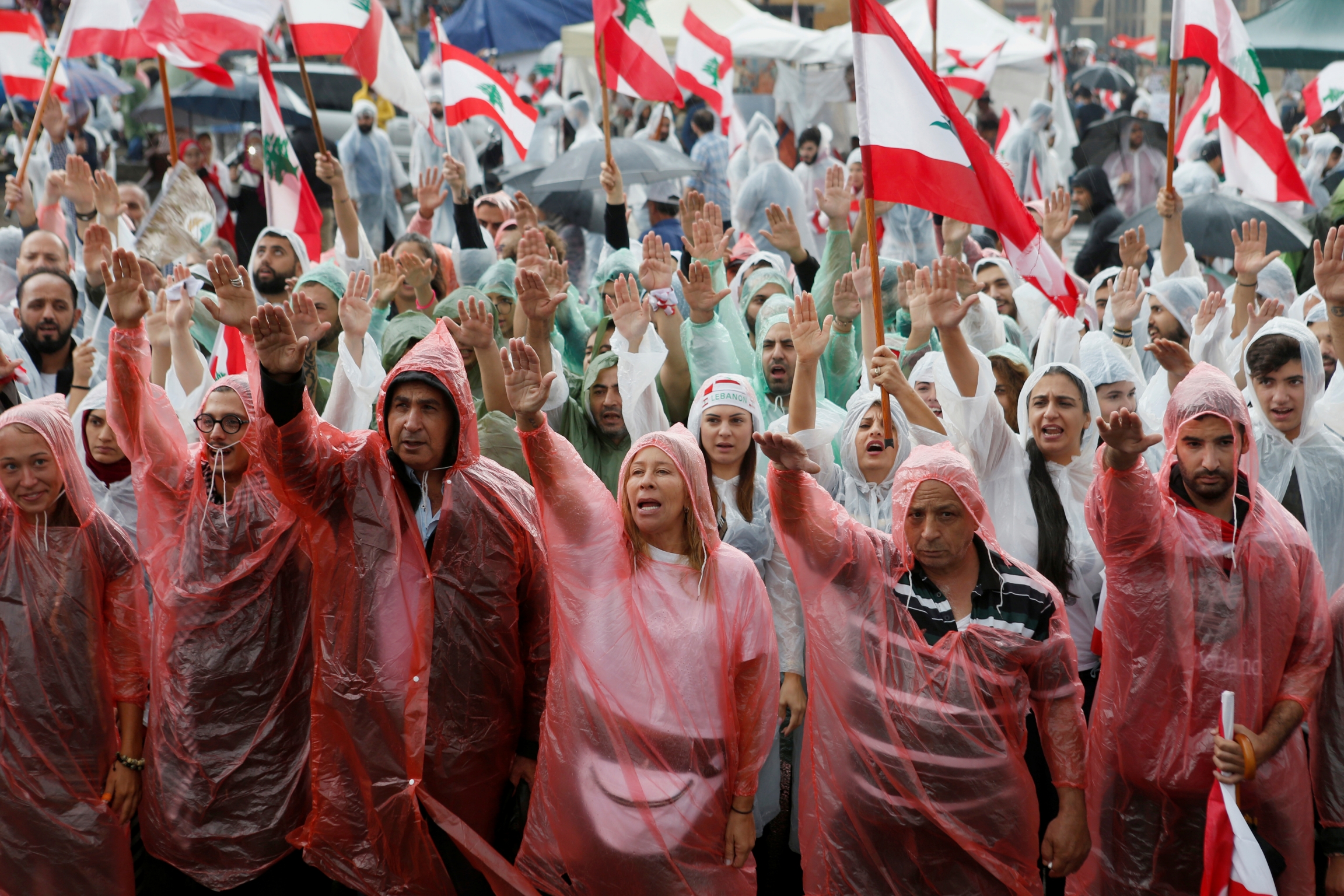 Demonstrators, covered in rain coats, gesture and carry flags during ongoing anti-government protests in downtown Beirut, Lebanon, Oct. 24, 2019. Demonstrators, covered in rain coats, gesture and carry flags during ongoing anti-government protests in downtown Beirut, Lebanon, Oct. 24, 2019.
