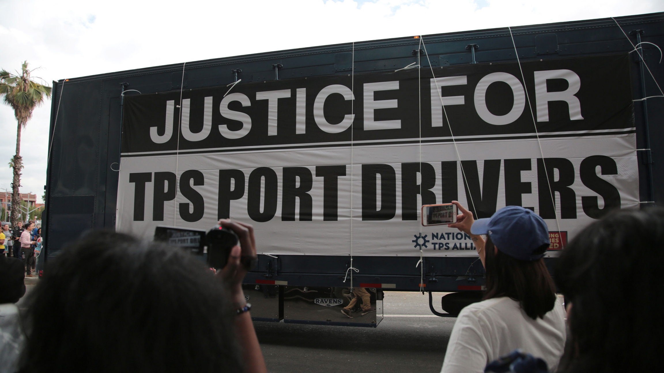 A large sign hanging off the side of a tractor reads "Justice for TPS Port Drivers"