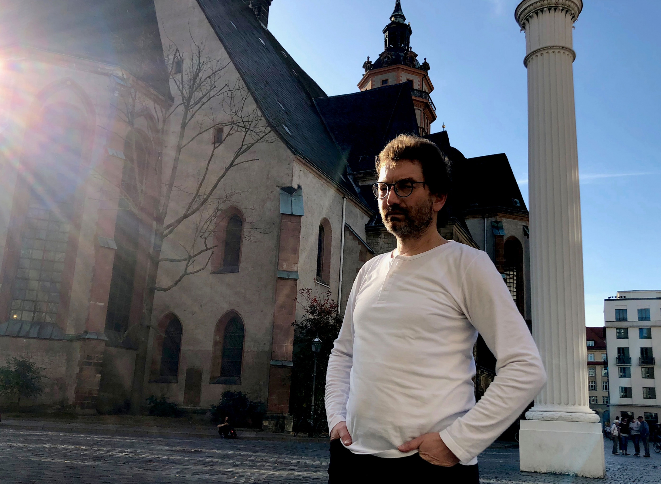 A man poses for a photograph. Behind him is a large old church.
