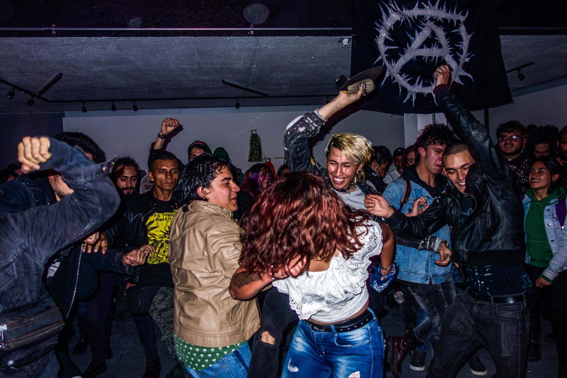 Concert-goers dance in a mosh pit at a punk concert in Bogotá. Concert-goers are shown throwing their bodies around at each other at a punk concert.