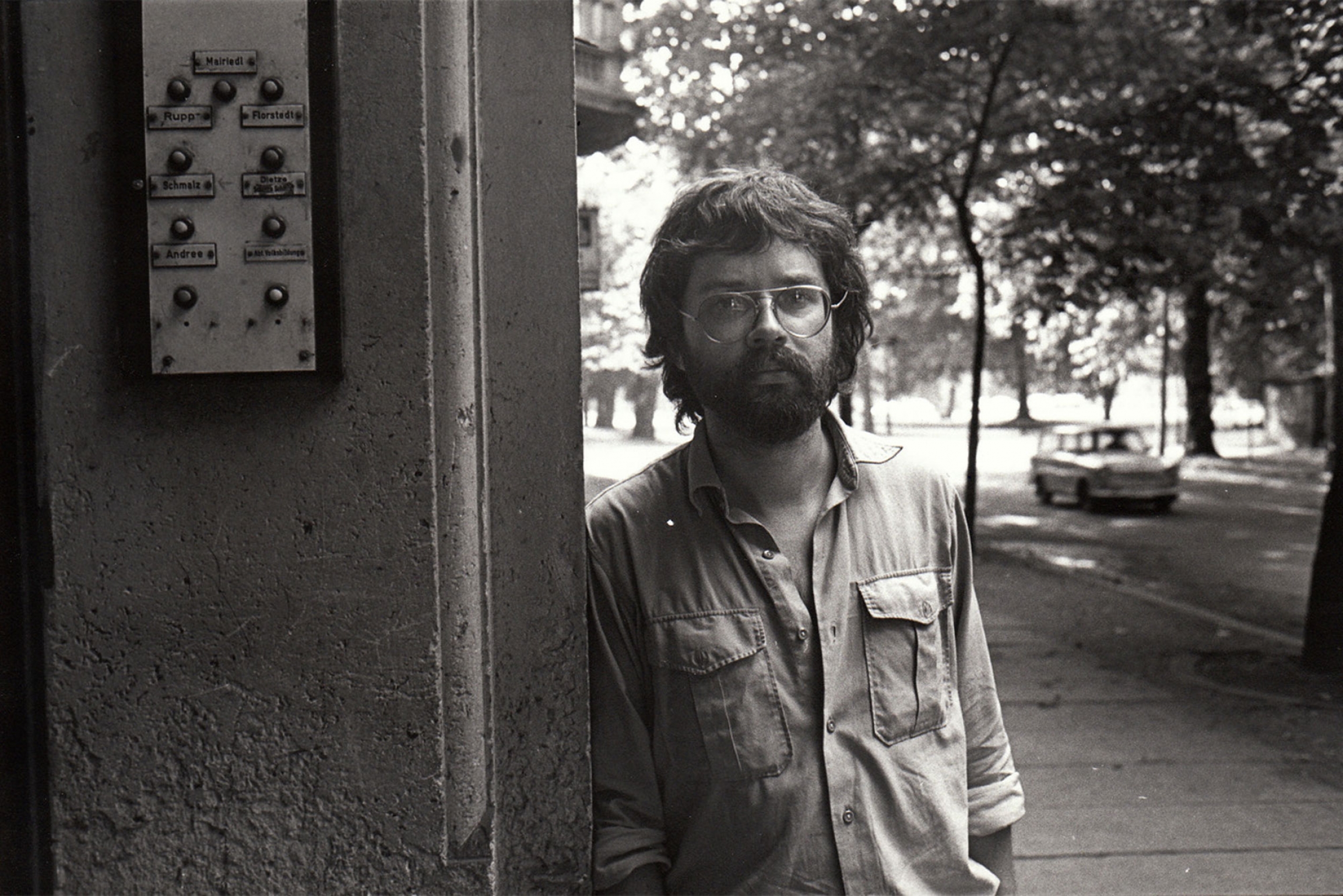 Andreas Voigt in 1986 during shooting of his first film, "Alfred." Andreas Voigt is shown leaning next to a building and wearing glasses.