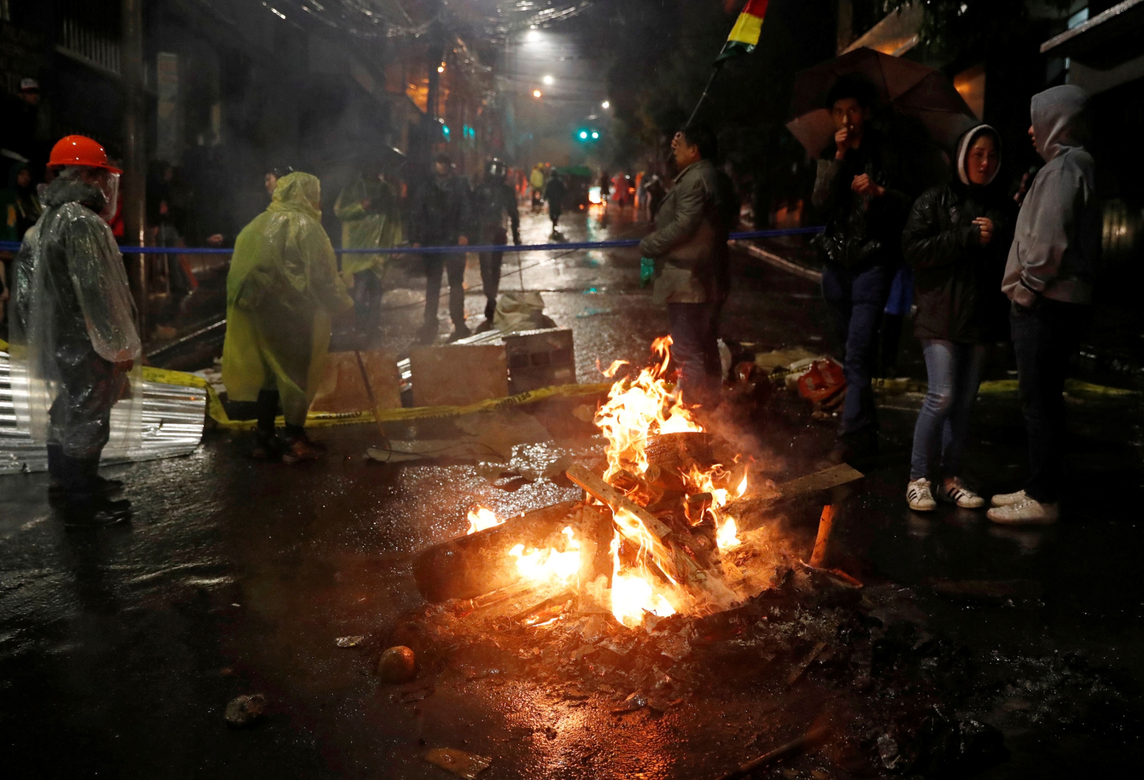 Demonstrators stand around a burning barricade during a protest against Bolivia's President Evo Morales in La Paz, Bolivia, Nov. 10, 2019. Several people are shown in the street standing around a large fire and wearing rain ponchos.