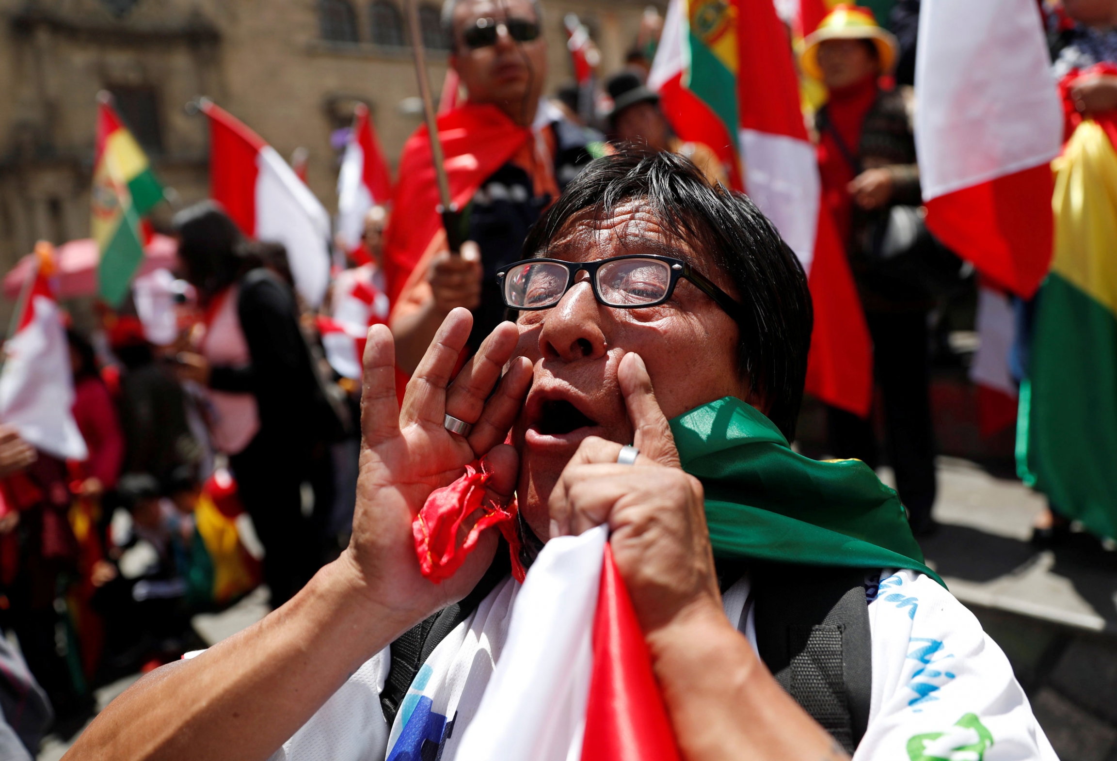 A demonstrator shouts during a protest in La Paz, Bolivia, Nov. 10, 2019. A demonstrator is shown with their hands around their mouth shouting and holding a Bolivian flag.