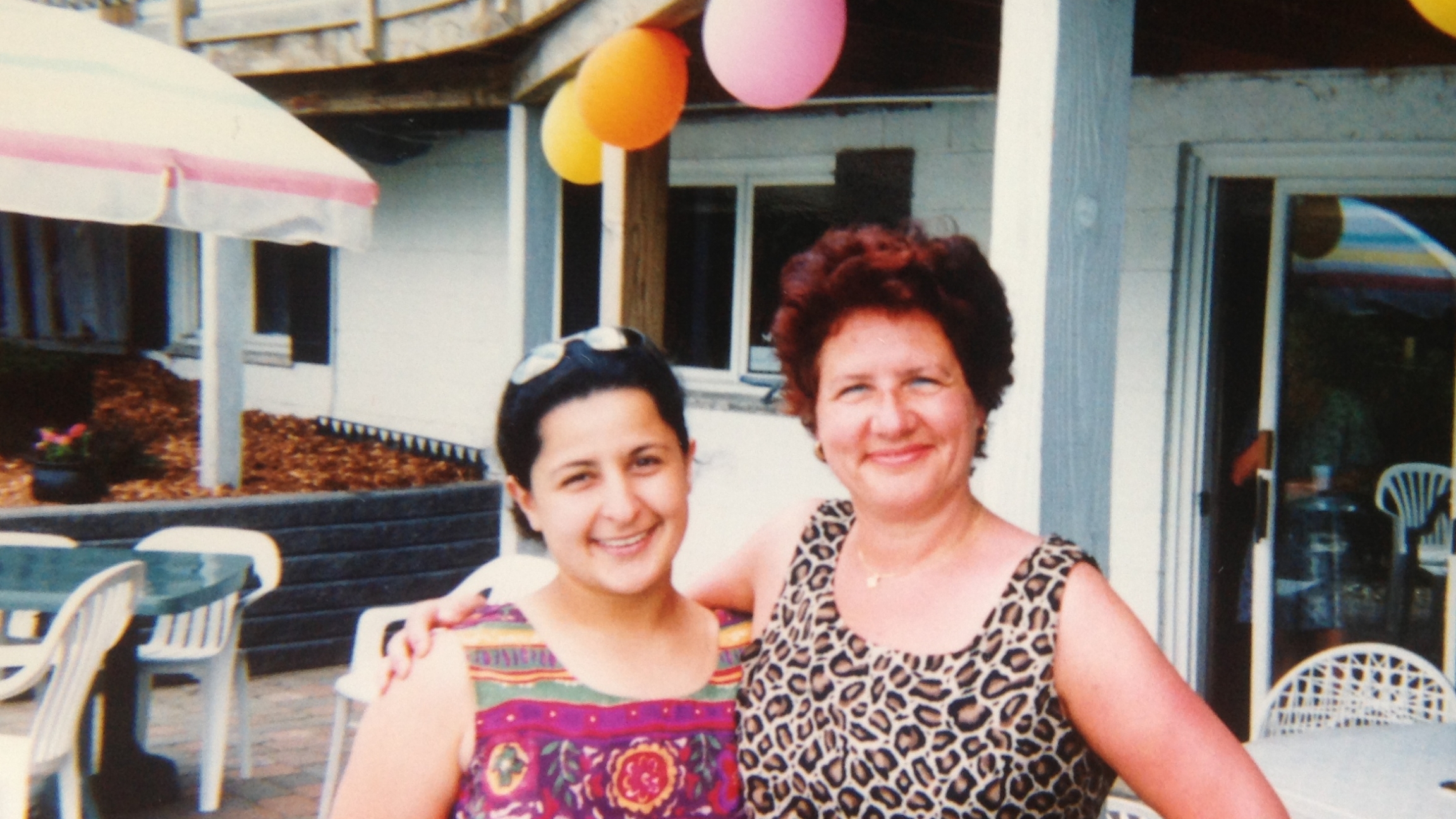 Nadia Neubacher (left) with her mom, Chantal Monté, during a visit to Michigan in 2003. A young woman stands next to her mother with colorful balloons in a backyard.