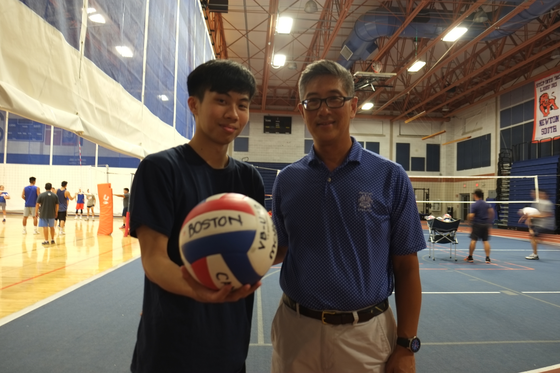 Ethan Wong and his father,John Wong, each started playing 9-man when they were 13 years old. John now coaches a 9-man team. A young Asian man and older Asian man stand next to each other with a volleyball