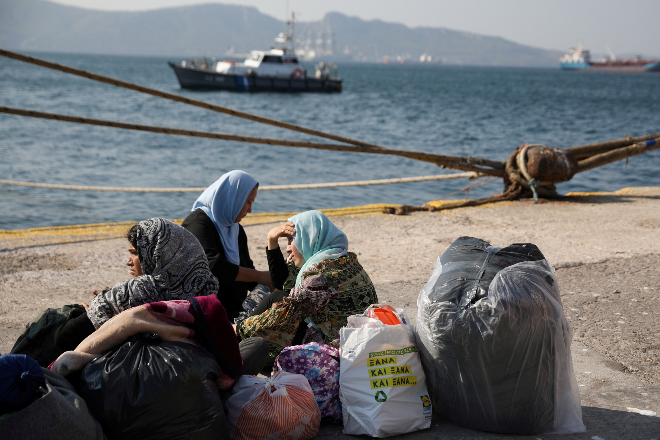 Refugees and migrants wait to be transferred to camps on the mainland, at the port of Elefsina near Athens, Greece, Oct. 22, 2019. A group of women wearing head scarves sit near their luggages and bags at a port