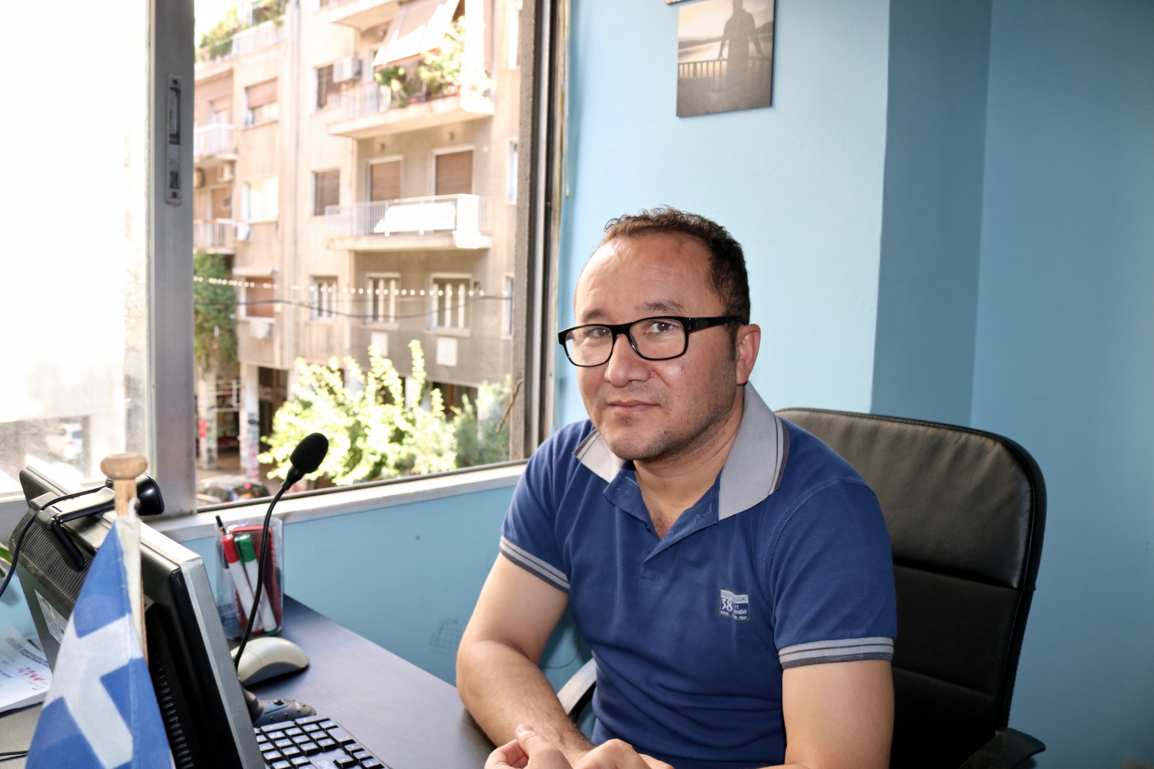 A man wearing a blue shirt and glasses sits at his desk