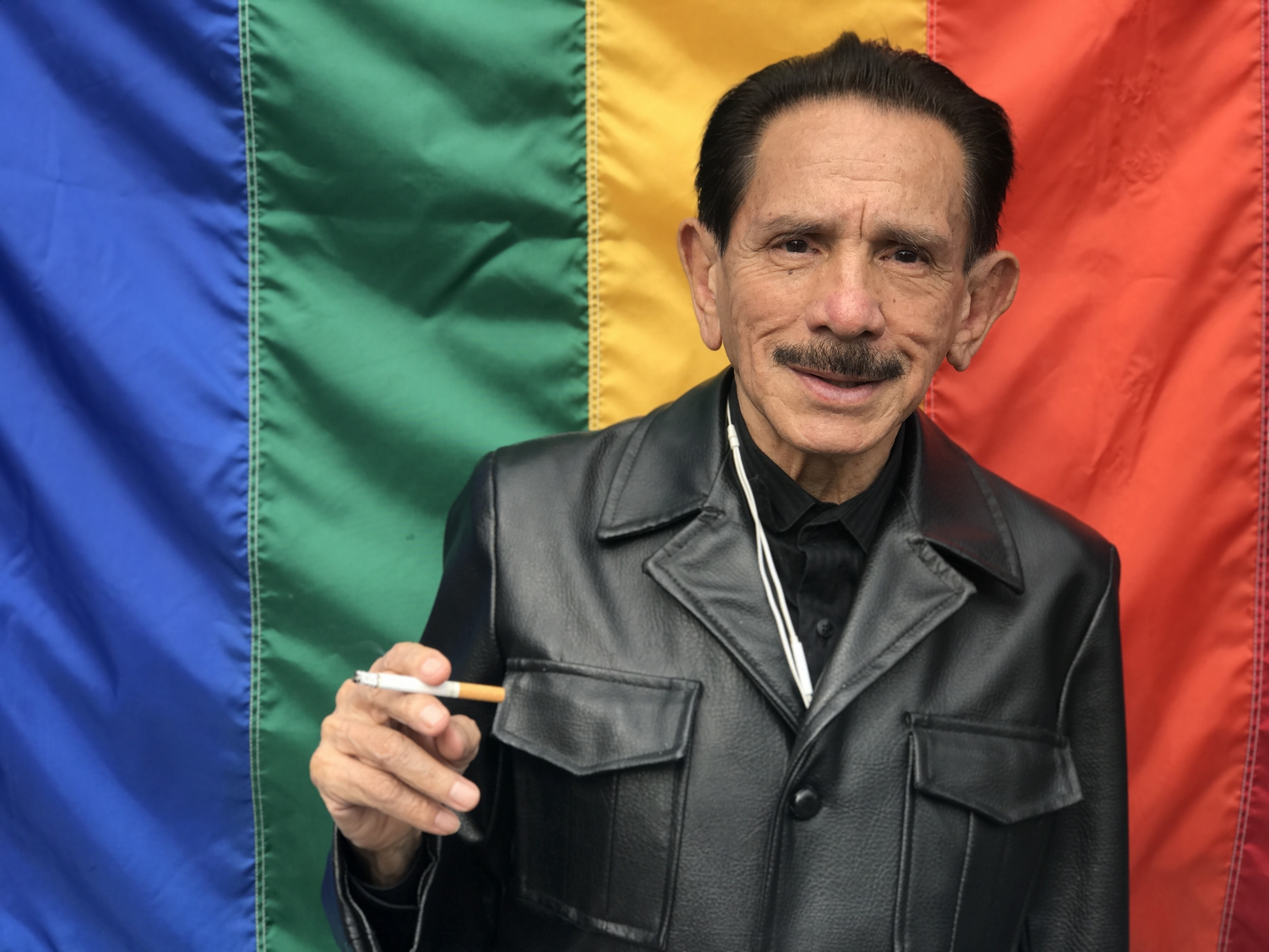 Gustavo Pérez, 80, smokes a cigarette in front of a rainbow flag outside Vida Alegre, Mexico City, Mexico. A man wearing a leather vest smokes in front of rainbow flag