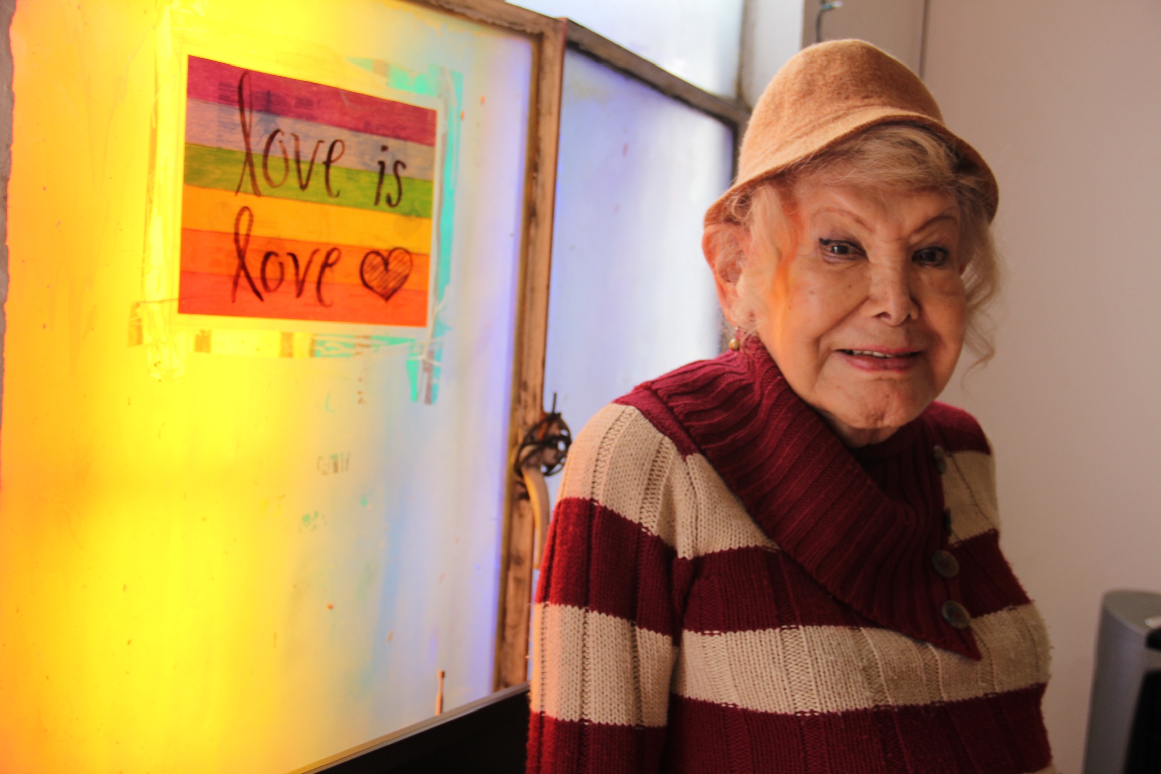 Samantha Flores cofounded Vida Alegre, a house for LGBTQ seniors, about a year ago, after having worked with children for many years. A woman stands next to rainbow sign that says love is love