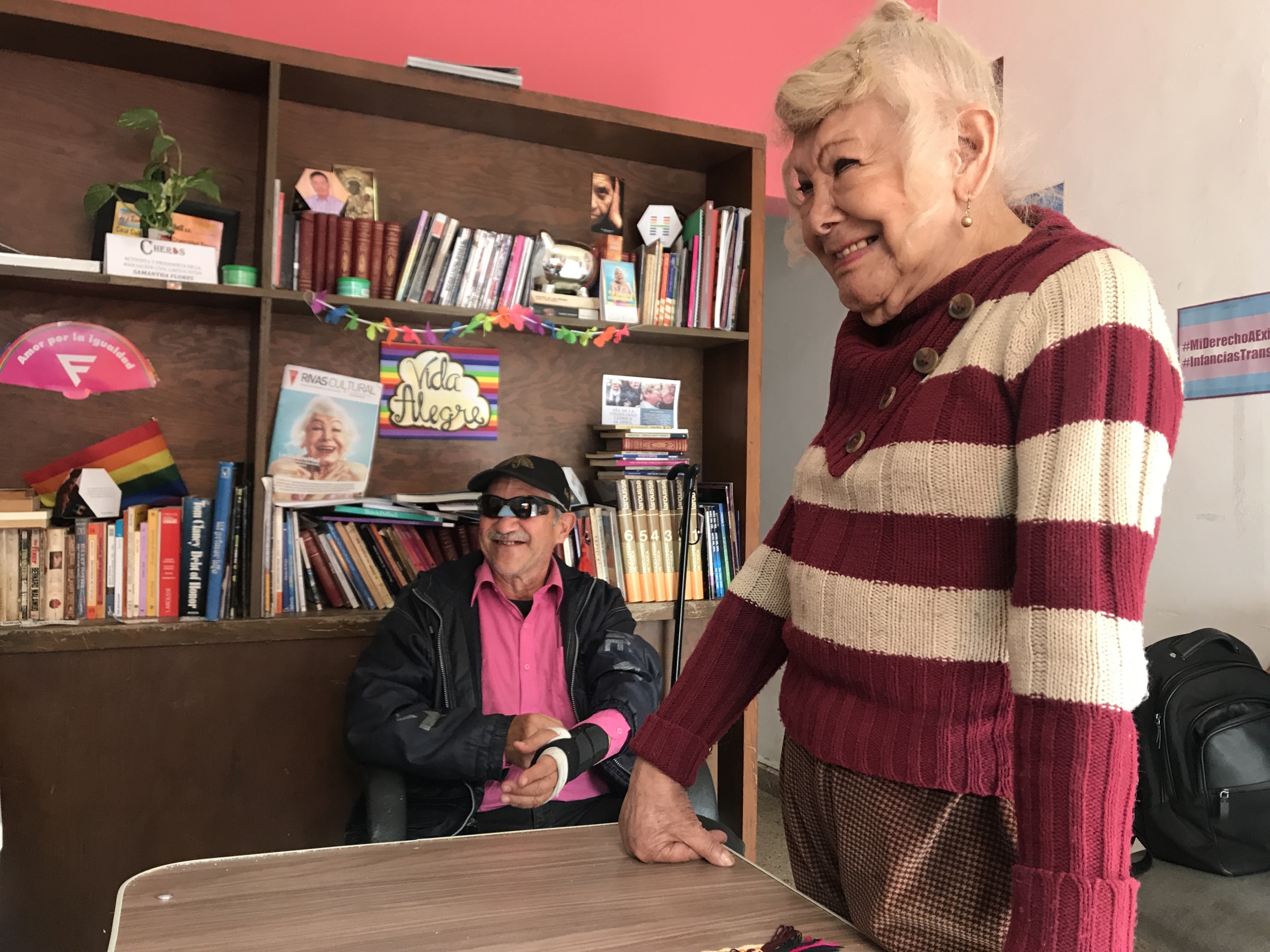 Samantha Flores, 87, enjoys her time talking to Vida Alegre members. A woman talks with friends in a center near a bookshelf