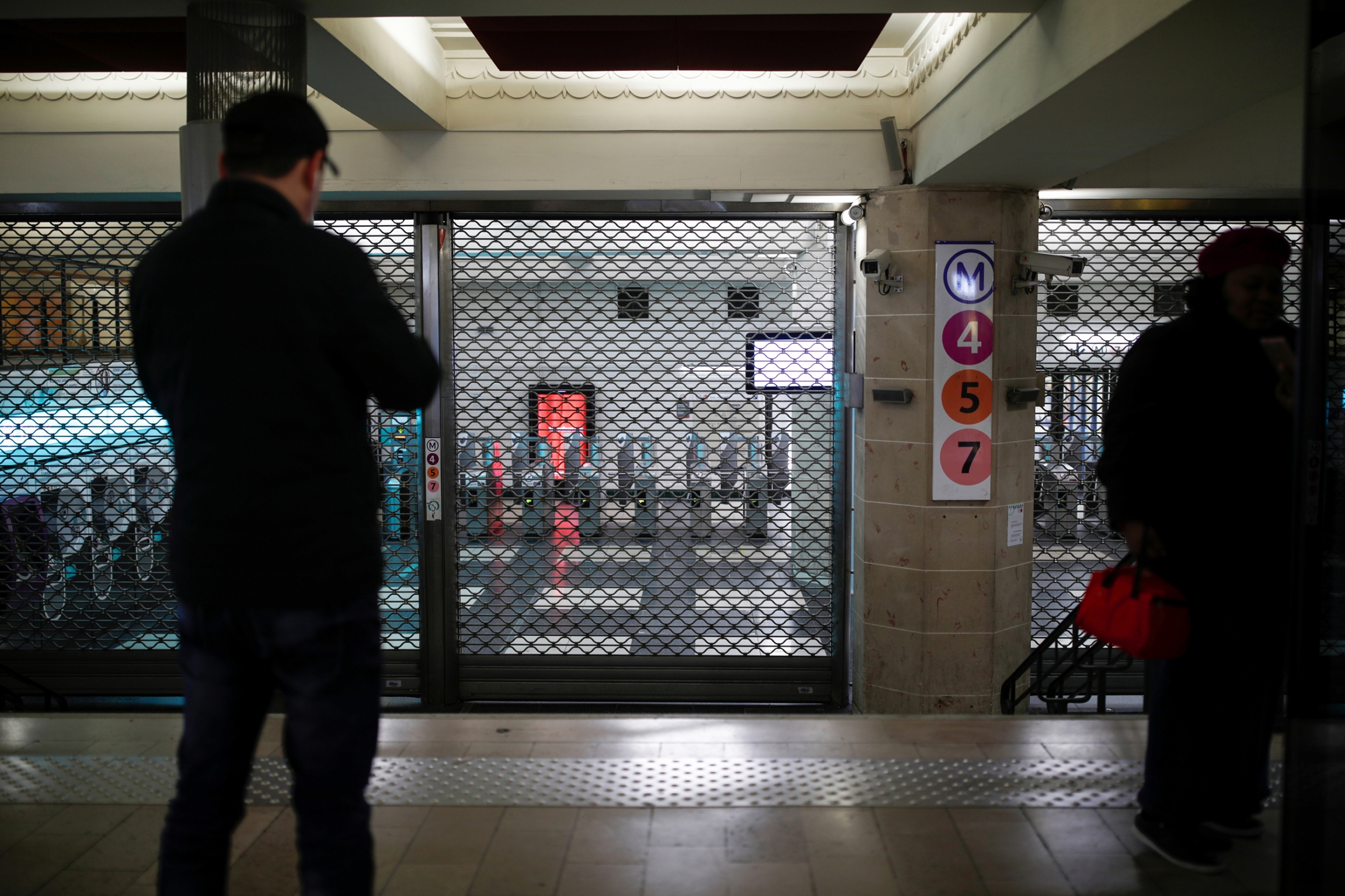 A closed entrance at the Gare de l'Est metro station is seen during a strike by French railway workers, Dec. 5, 2019. Metal gates block a closed entrance at the Gare de l'Est metro station with a man standing in shadow in the nearground looking on.