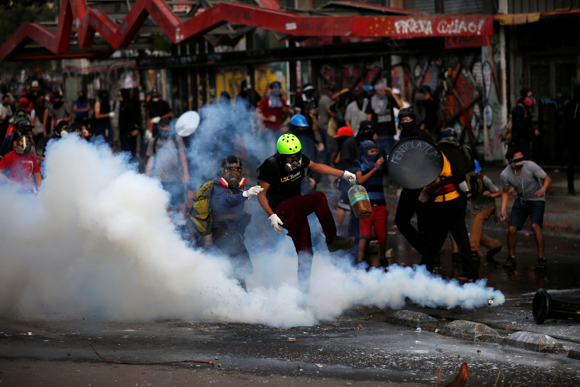 Demonstrators react amid tear gas during a protest against Chile's government in Santiago, Chile Dec. 10, 2019. A goupr of demonstrators wearing gas masks are show surrounded by clouds of tear gas.