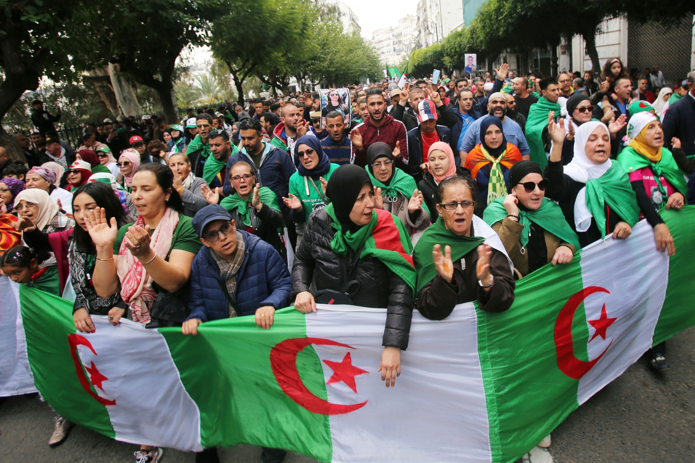 Demonstrators carry national flags and gesture during a protest rejecting the December presidential election in Algiers, Algeria, Nov. 22, 2019. A large group of demonstrators are shown filling a street in Algiers with the Algerian flag in front of them.