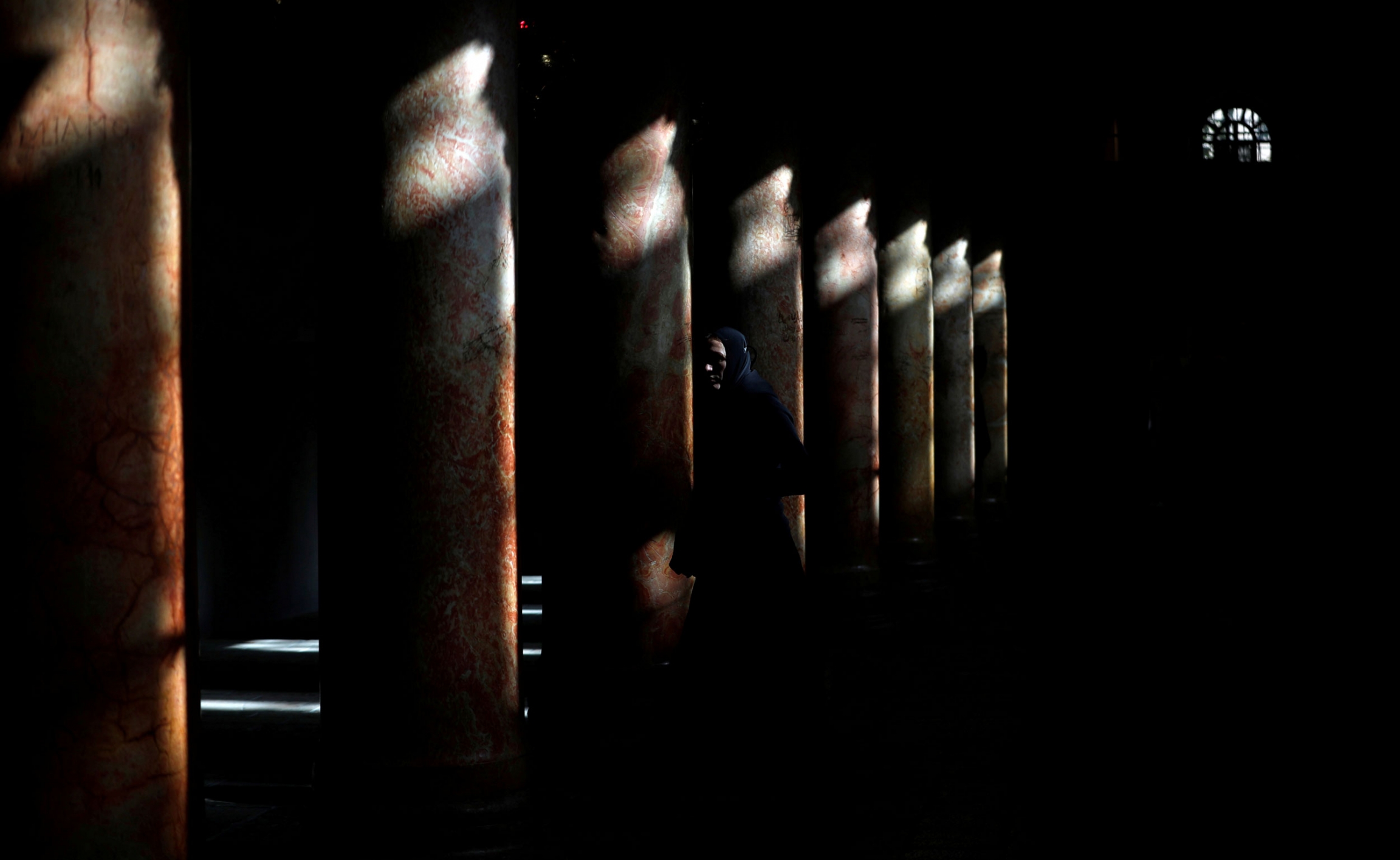 A worshipper walks inside the Church of the Nativity in Bethlehem, in the Israeli-occupied West Bank, on Jan. 6, 2019. A worshipper is shown inside of the Church of the Nativity with very little light coming in and shinning on the tops of a row of marble columns.