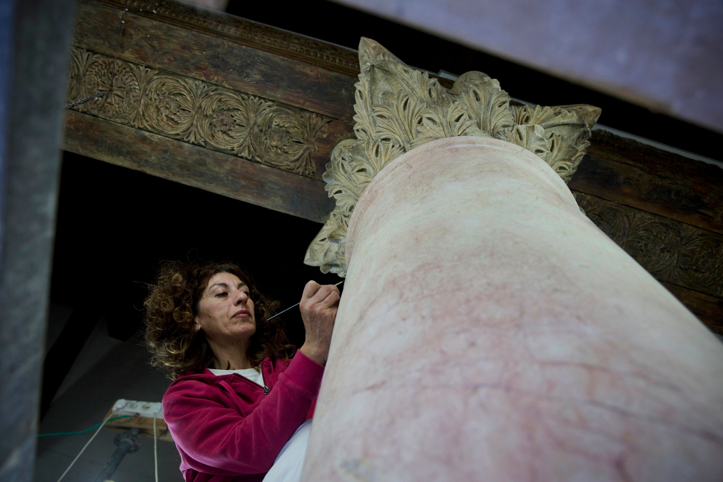 A restoration expert works on a granite column inside the Church of the Nativity on Dec. 6, 2018. A woman is shown wearing a purple sweater and holding a small brush performing restoration on a granite column.