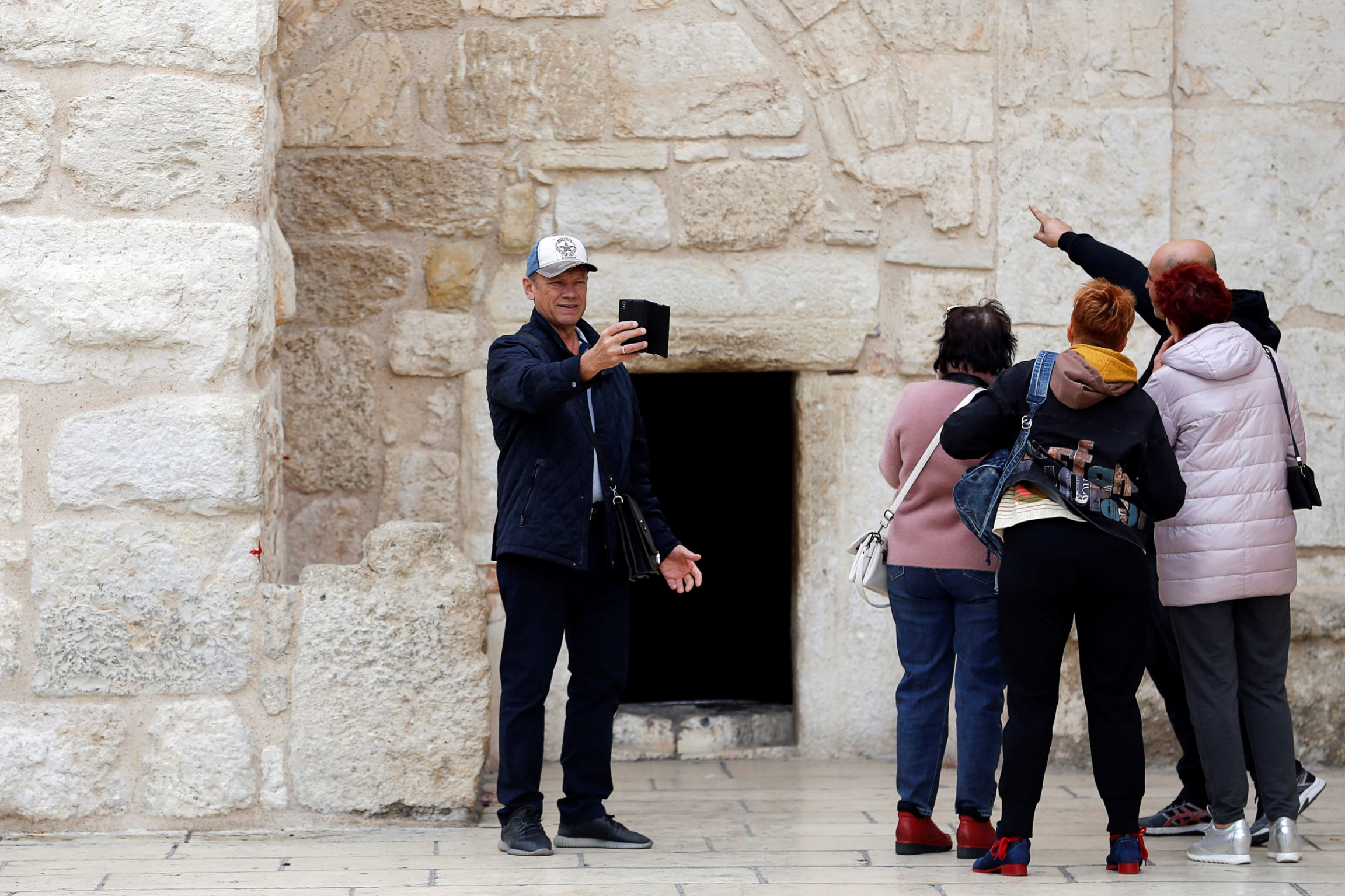 A tourist takes a selfie outside the Church of the Nativity in Bethlehem, in the Israeli-occupied West Bank on Dec. 2, 2019. A tourist wearing a ball cap is shown with four other tourists taking a selfie outside the Church of the Nativity.