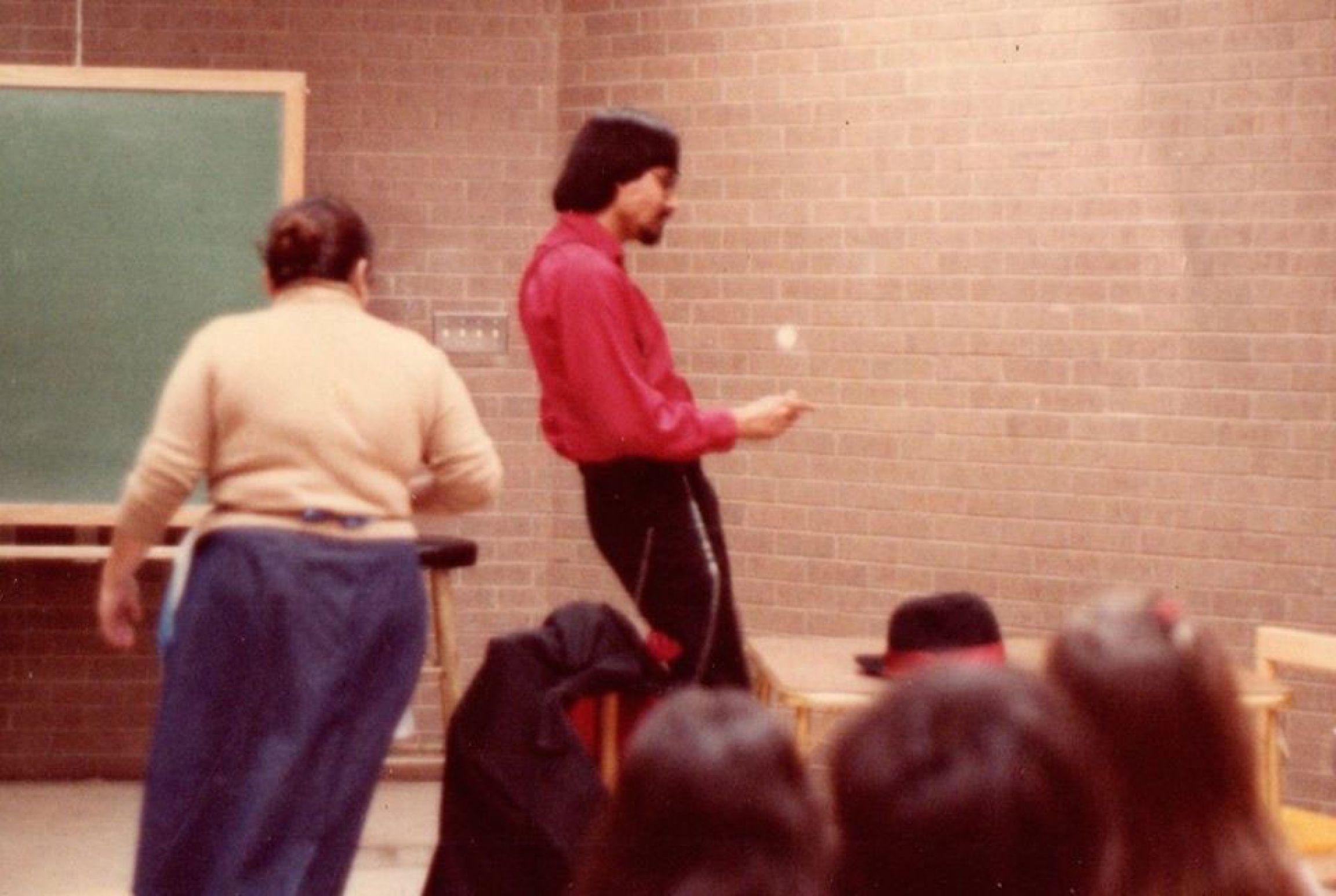 Pancho Claus started with a play written by Richard Reyes in 1981. Pancho Claus is shown in a red shirt on a stage with a brick background.