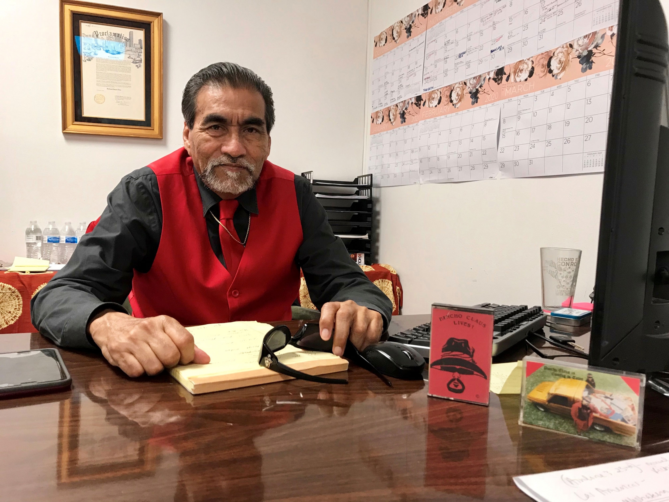 Richard Reyes sits at his desk at Talento Bilingue de Houston. Richard Reyes is shown wearing a red vest and tie while sitting at his desk