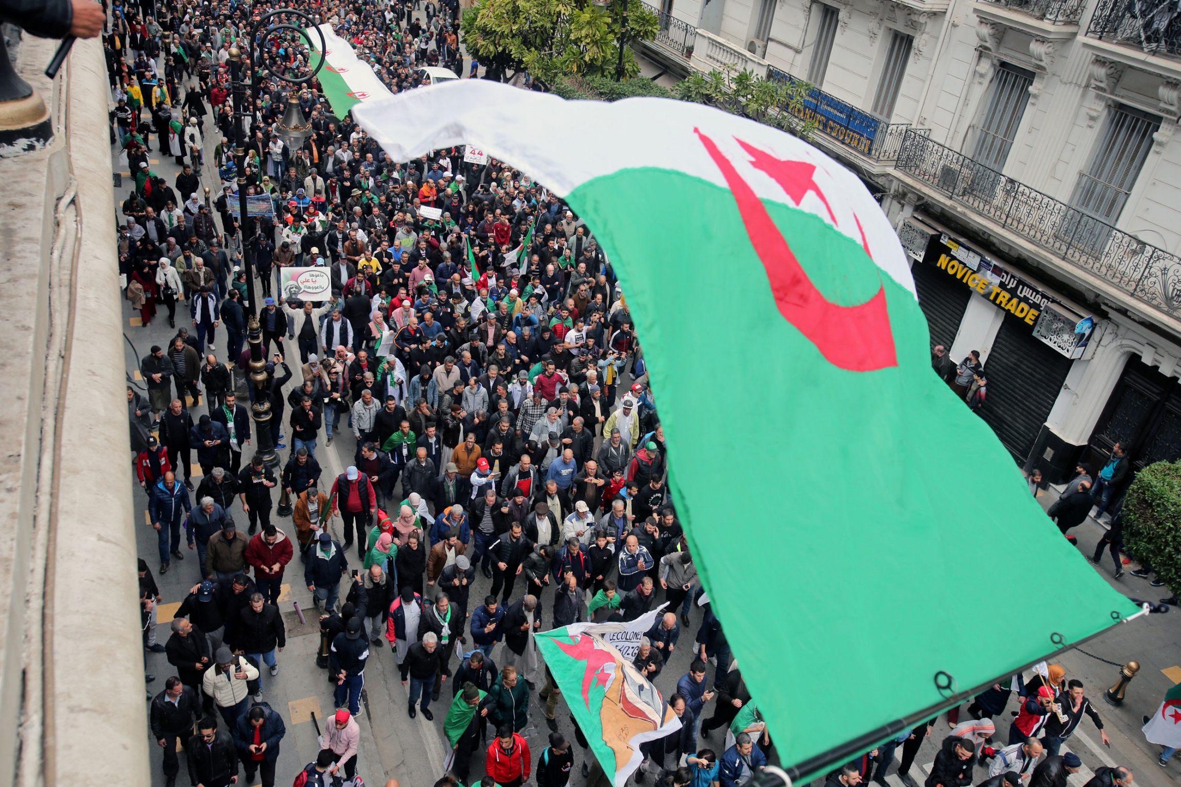 Demonstrators carry a national flag during a protest to reject the presidential election result in Algiers, Algeria, Dec. 20, 2019. A street is shown filled with people and an Algerian flag is in the nearground.
