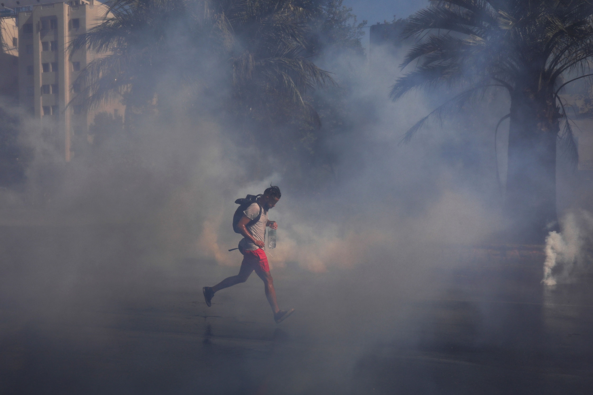 A demonstrator runs amid tear gas during a protest against Chile's government in Santiago, Chile, Dec. 27, 2019. A demonstrator wearing red shorts and carrying a backpack, runs amid tear gas.