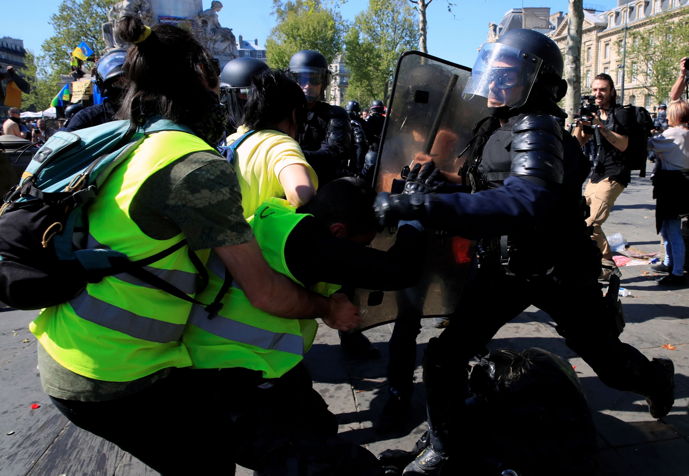 A protester scuffles with a police officer during a demonstration of the yellow vests movement in Paris, France, April 20, 2019. Two people wearing yellow safety vests are shown on one side with a police officer on the other carrying a shield.