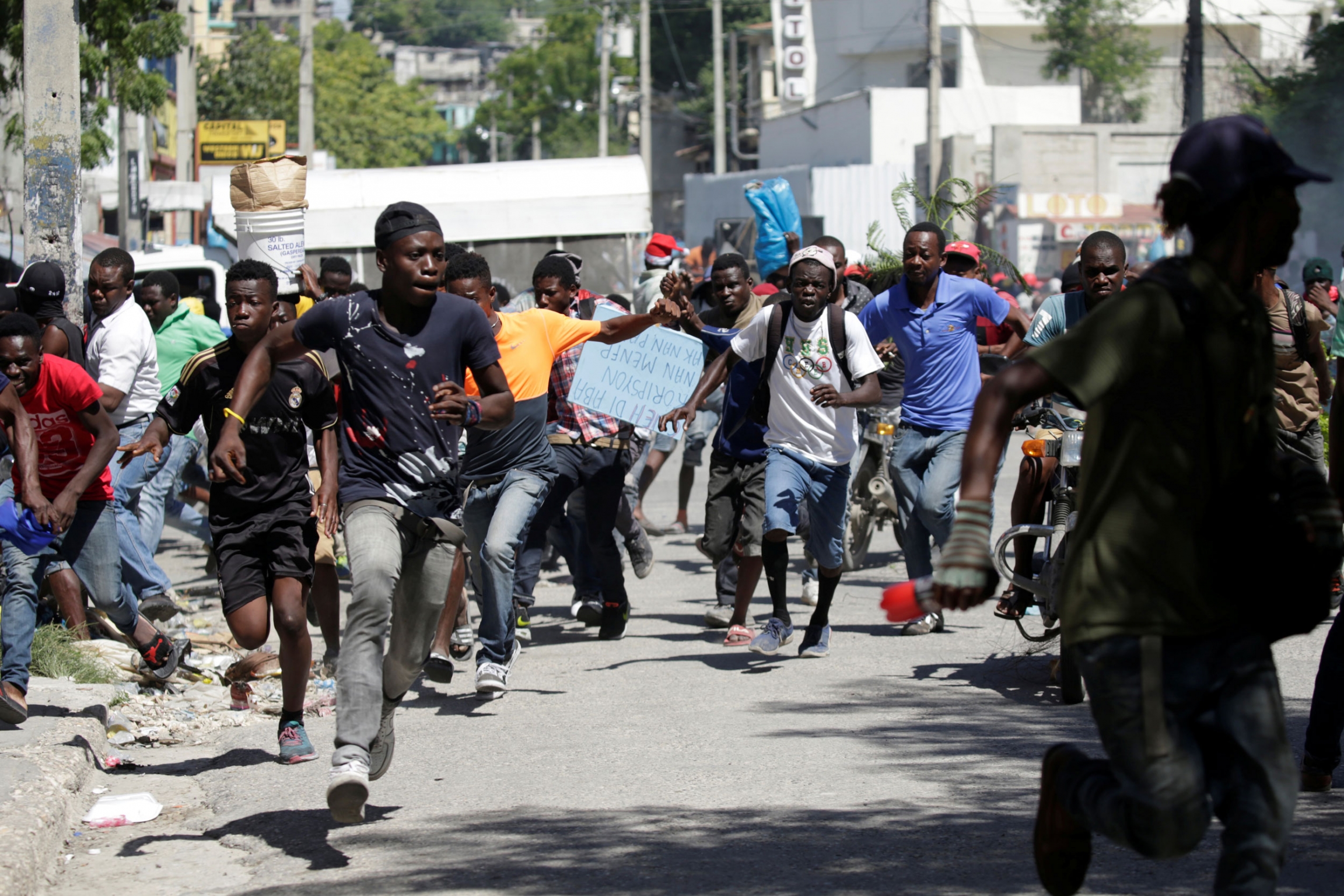 Protesters run away as Haitian National Police officers disperse them during a protest demanding the resignation of Haitian President Jovenel Moise, in the streets of Port-au-Prince, Haiti Oct. 28, 2019. A large group of protesters are shown running in the street.