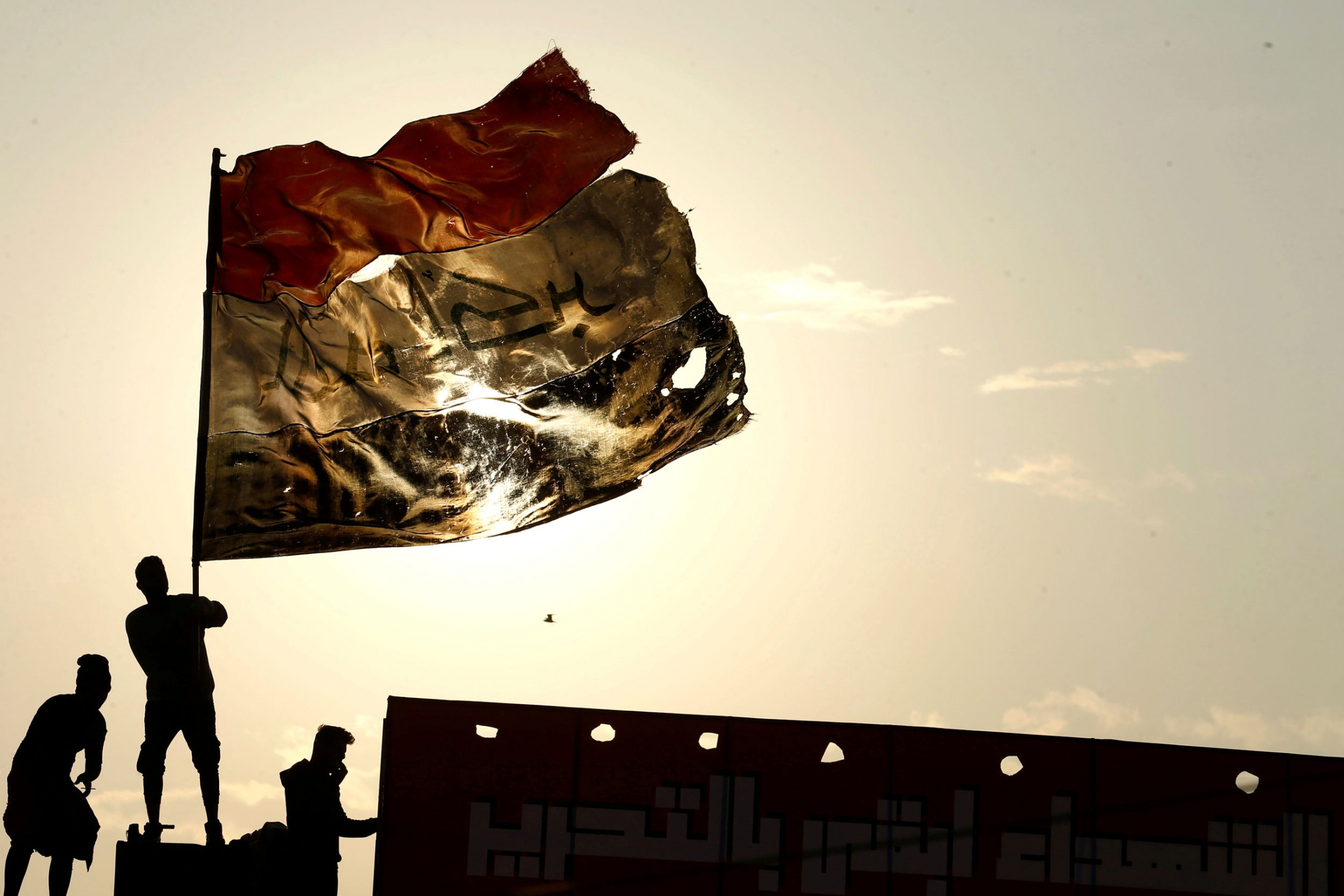 An demonstrator carries an Iraqi flag during ongoing anti-government protests, in Baghdad, Iraq, Dec. 10, 2019. Three people are shown with one holding a large tattered Iraqi flag