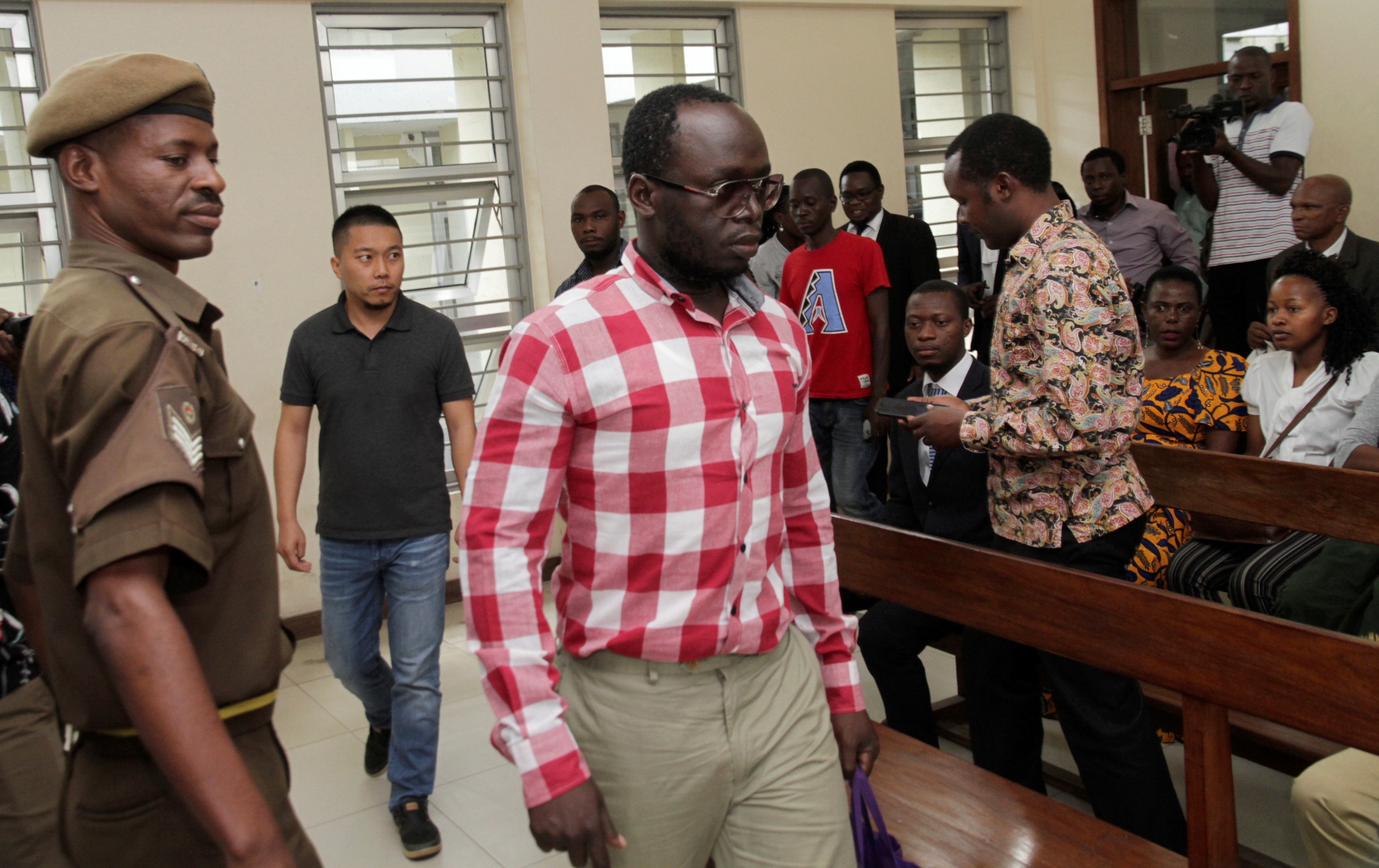 Tanzanian investigative journalist Erick Kabendera arrives at the Kisutu Residents Magistrate Court in Dar es Salaam, Tanzania Aug. 19, 2019. Erick Kabendera wears a white and red shirt and leaves a court room flanked by police