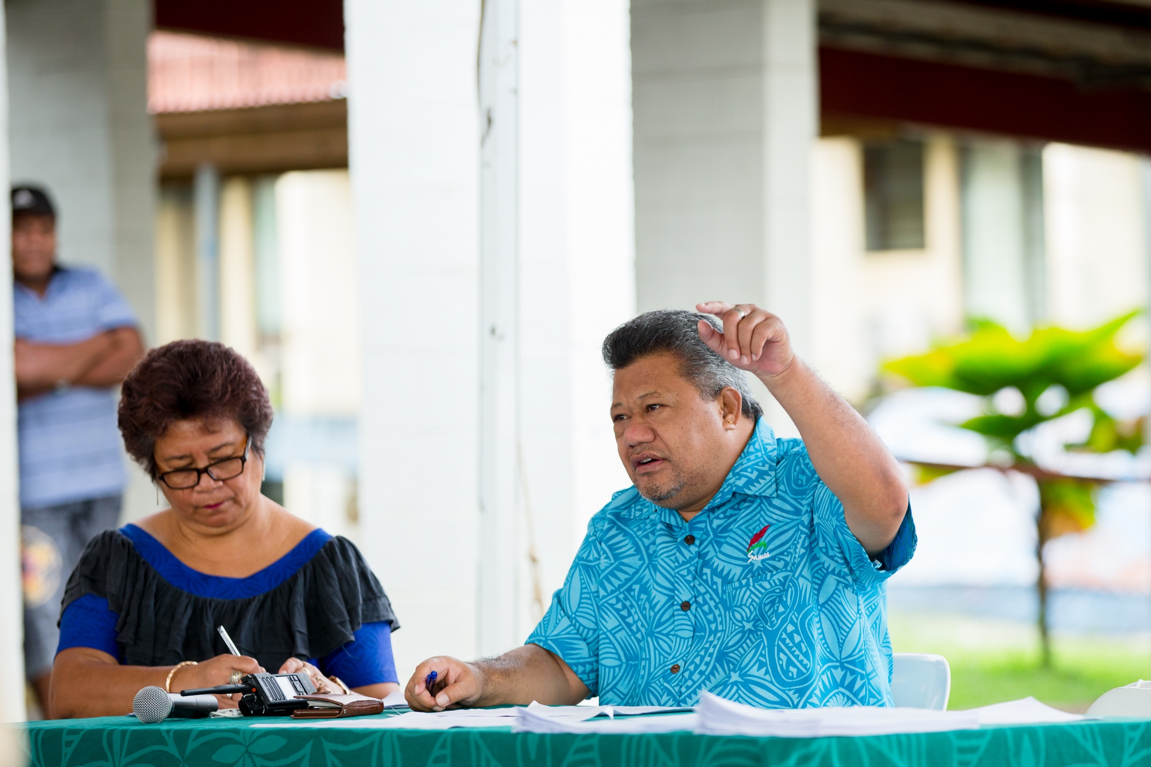 On Dec. 2, 2019, Dr. Take Naseri, (right) director general of health for the Samoa Ministry of Health, briefs nurses and vaccination teams in preparation for the UNICEF-supported national vaccination campaign in response to the current measles outbreak in A man wearing a blue shirt speaks and points his finger in the air, sits next to a woman