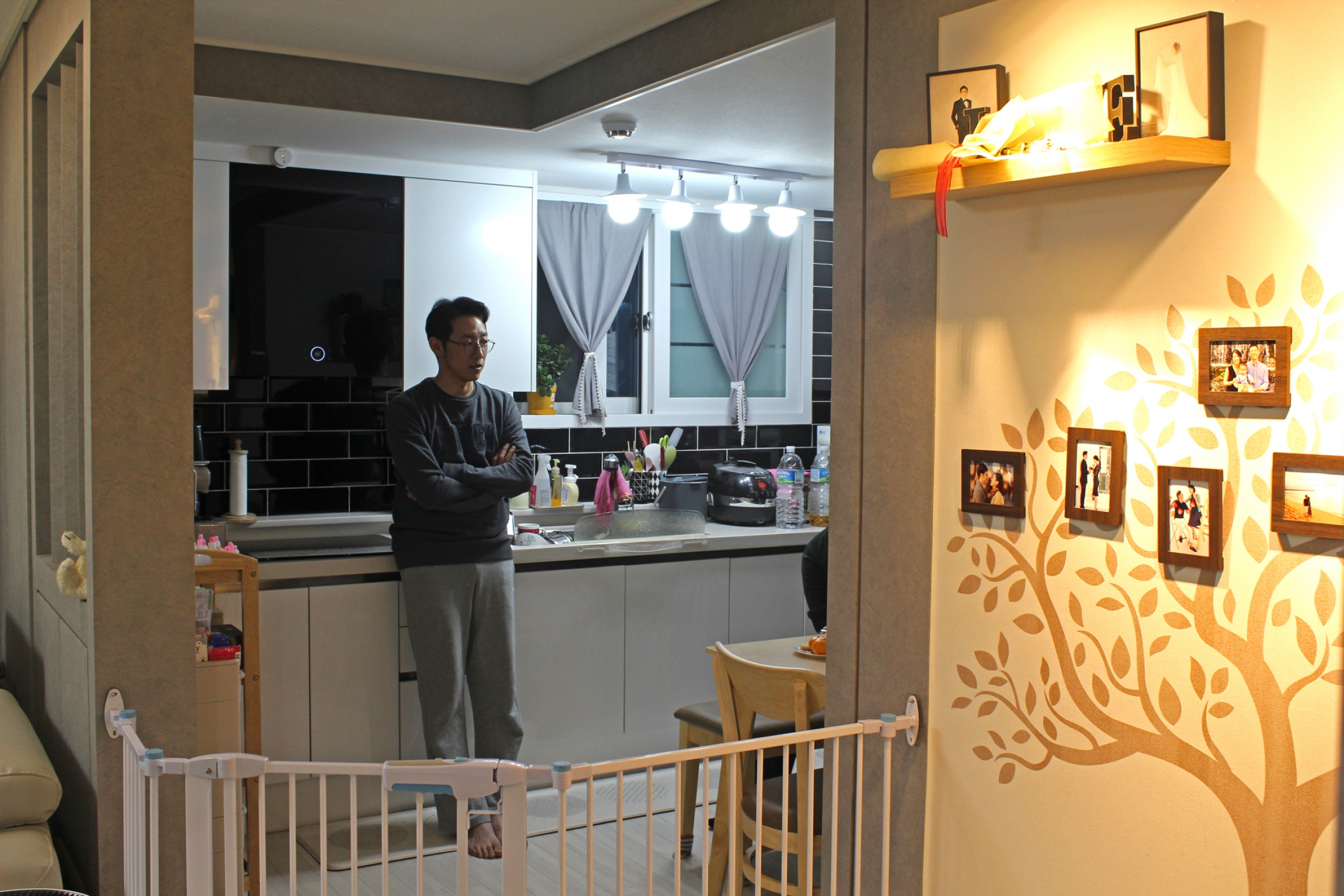 Cho Sung-won stands in his kitchen in his Seoul-area apartment, which he bought with help from the Seoul Metropolitan Government. A man stands in a low-lit kitchen with his arms crossed