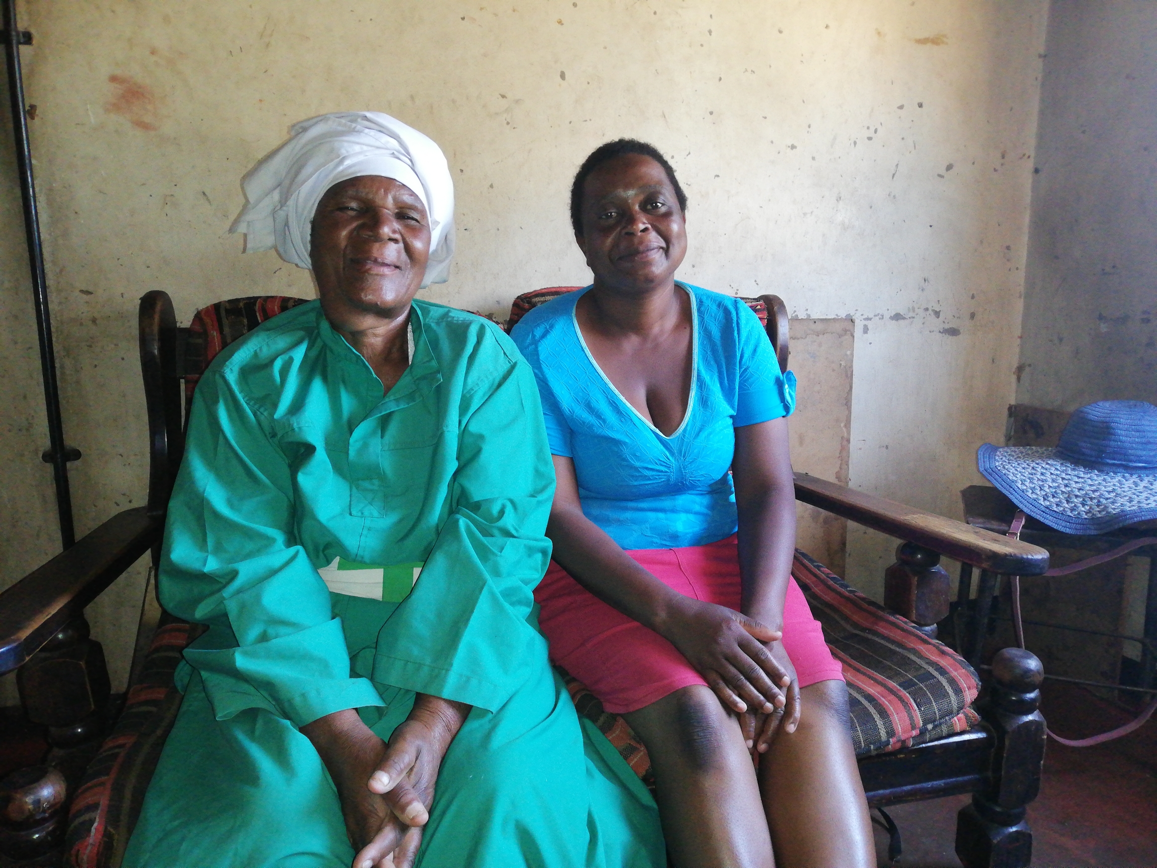 A traditional birth attendant, Esther Zinyoro (left) helps pregnant women who are being turned away from clinics who deliver at her home in what's known as "backyard" maternity wards. A woman wearing a green dress sits next to a woman wearing a blue shirt and pink skirt sit on a bench inside a clinic.