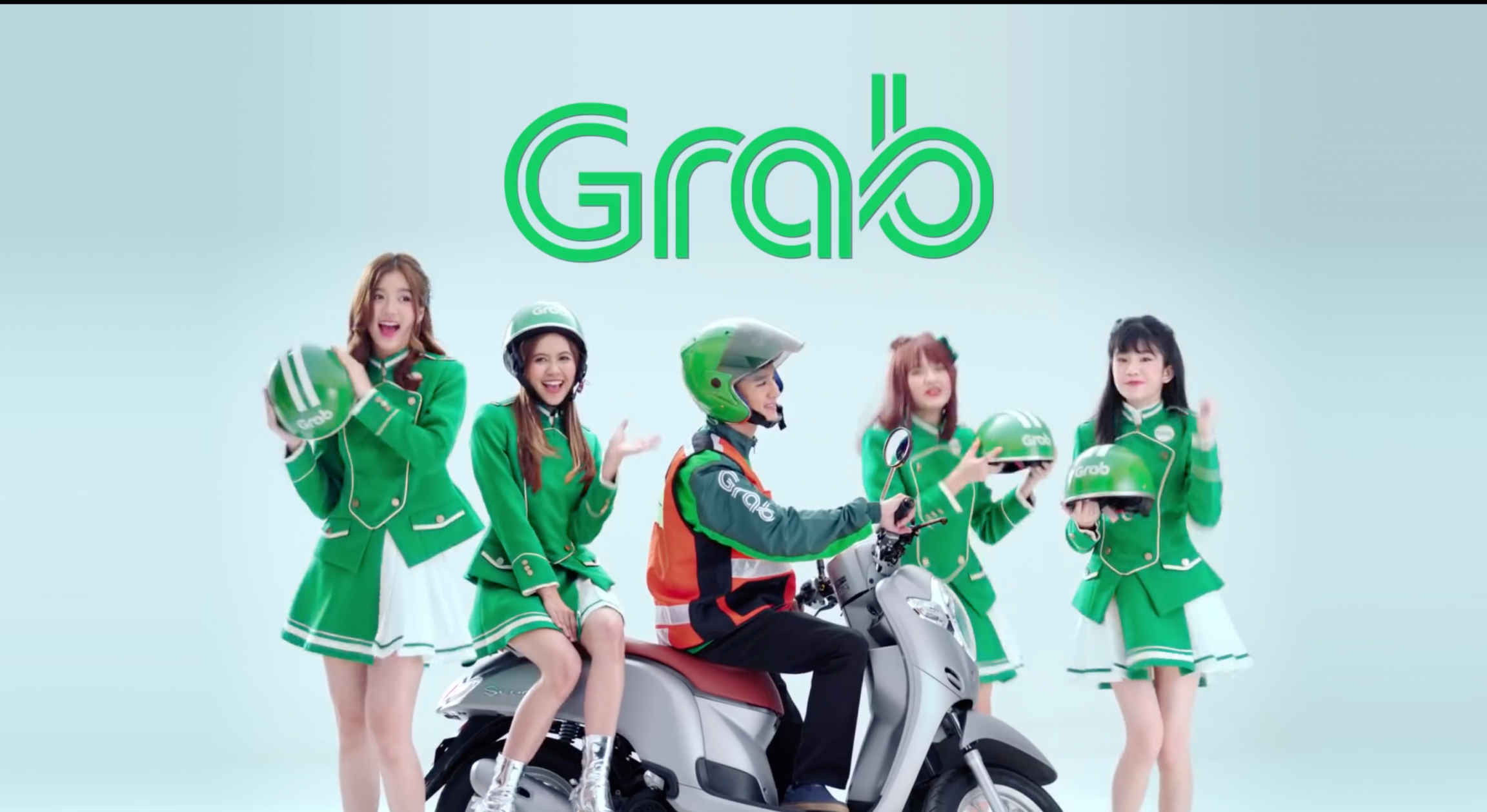 Screenshot of an ad on YouTube for GrabBike featuring BNK48, an extremely popular girl-pop ensemble from Bangkok, Thailand. A popular girl band poses near a Grab driver wearing green uniform