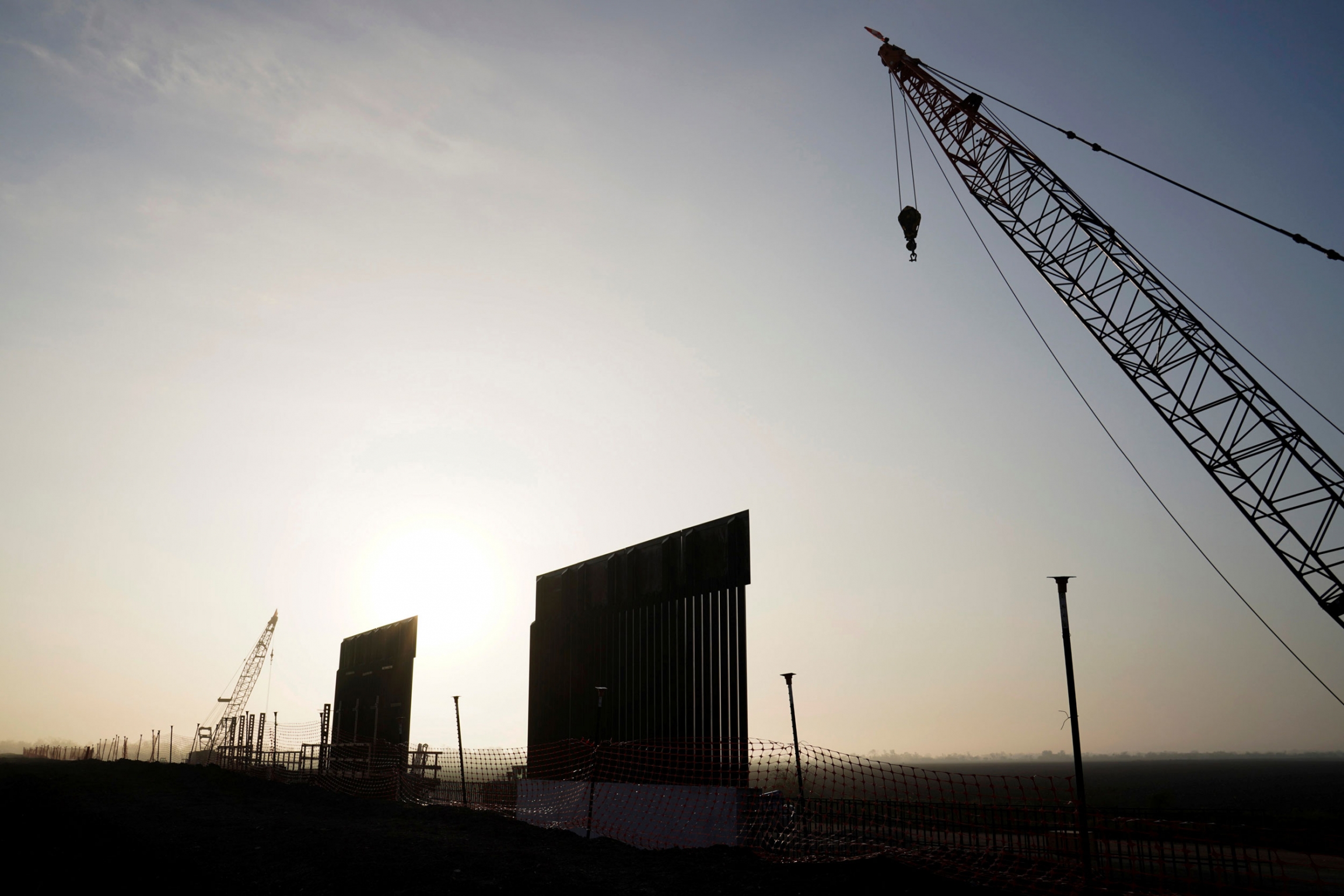 Segments of the first border wall in Texas since US President Donald Trump took office near Donna, Texas, Dec. 8, 2019. Two segments of the border wall are shown standing against a setting sun with a adjacent crane.