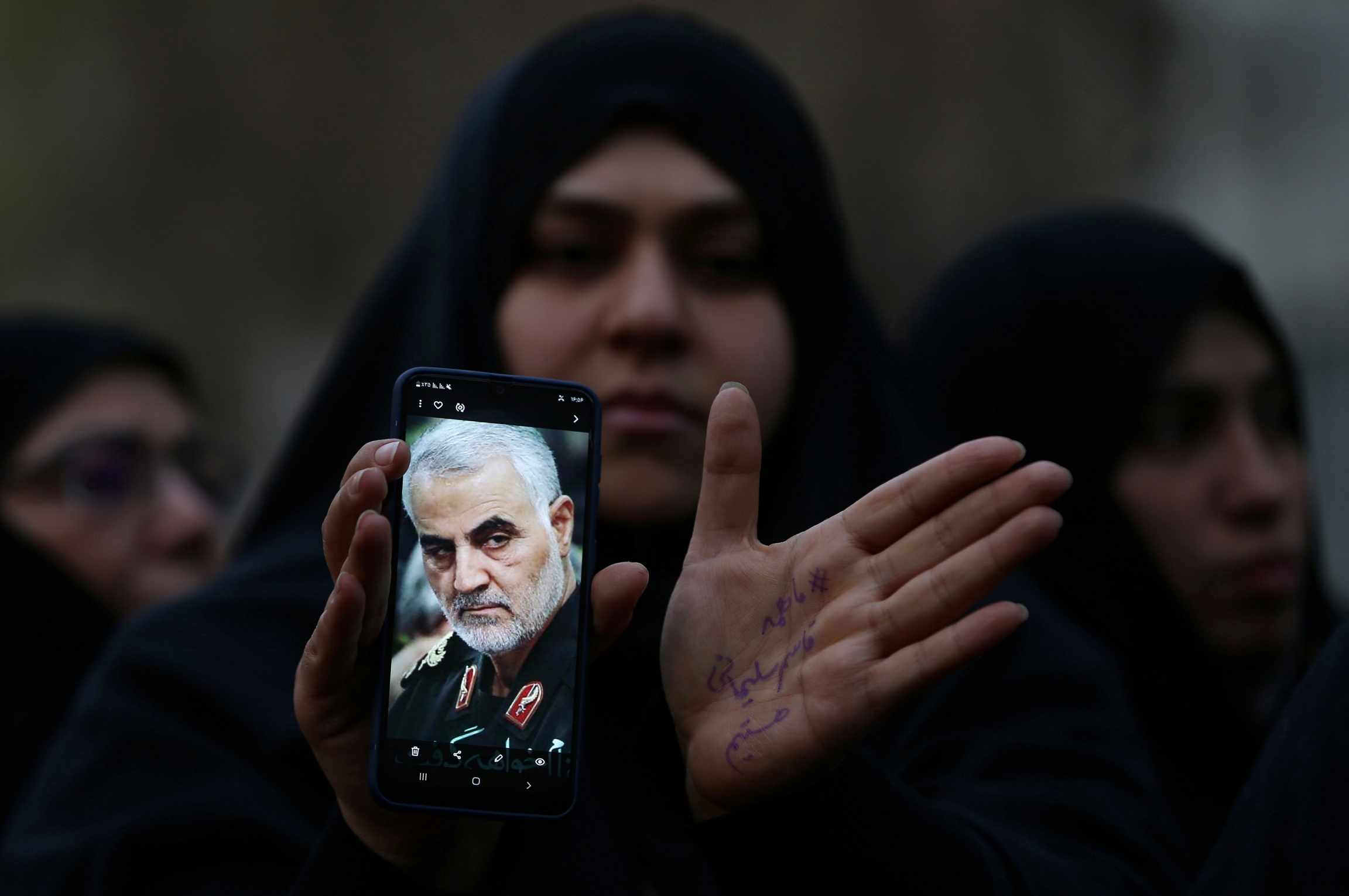 Tehran protests A woman wearing an abaya holds a cellphone with the photo of an Iranian military commander.