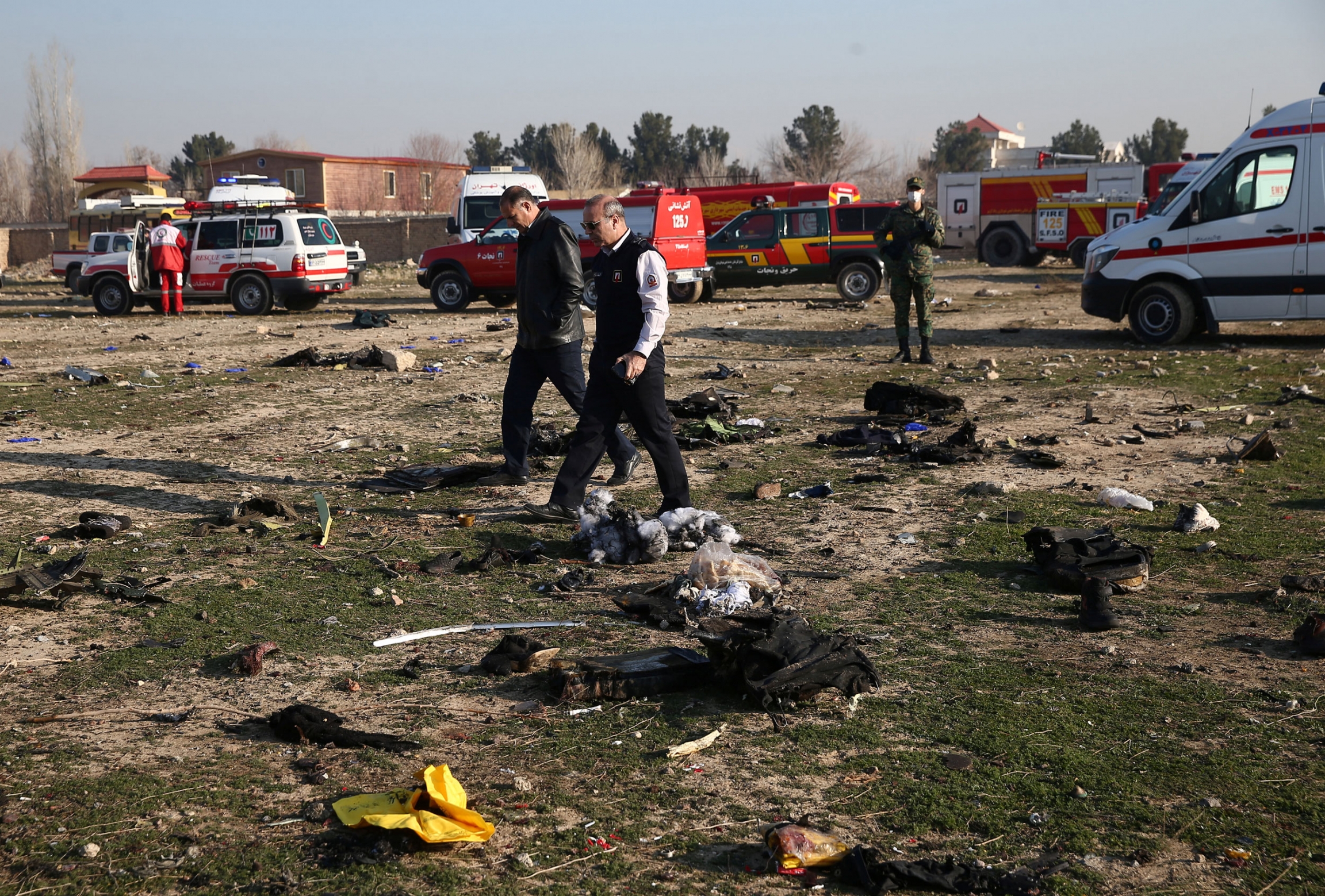 Emergency crew check the site where the Ukraine International Airlines plane crashed after take-off from Iran's Imam Khomeini Airport, on the outskirts of Tehran, Iran, Jan. 8, 2020. Two people are shown walking across a field strewn with reminant of a plane crash with several emergency vehicles in the background.