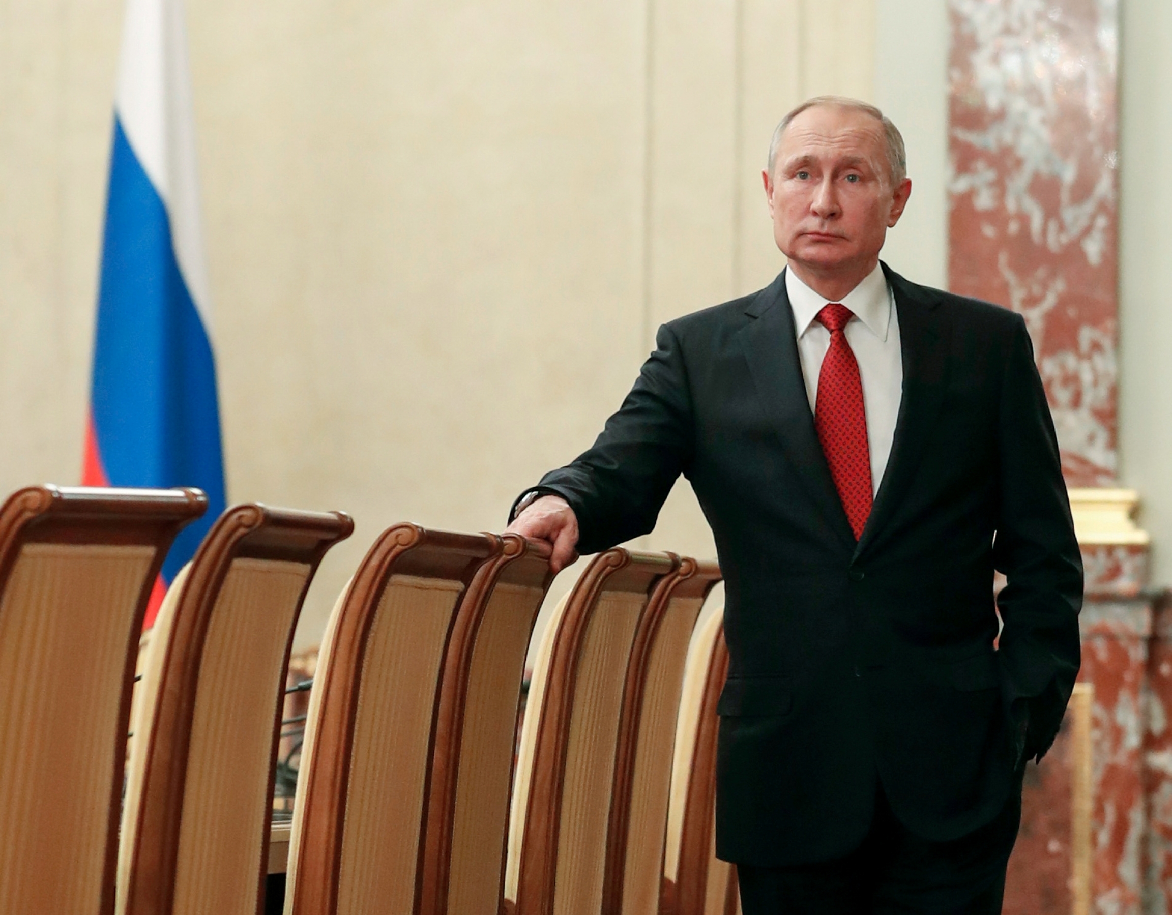 Vladimir Putin A man on a black suit and red tie stands in a meeting room.