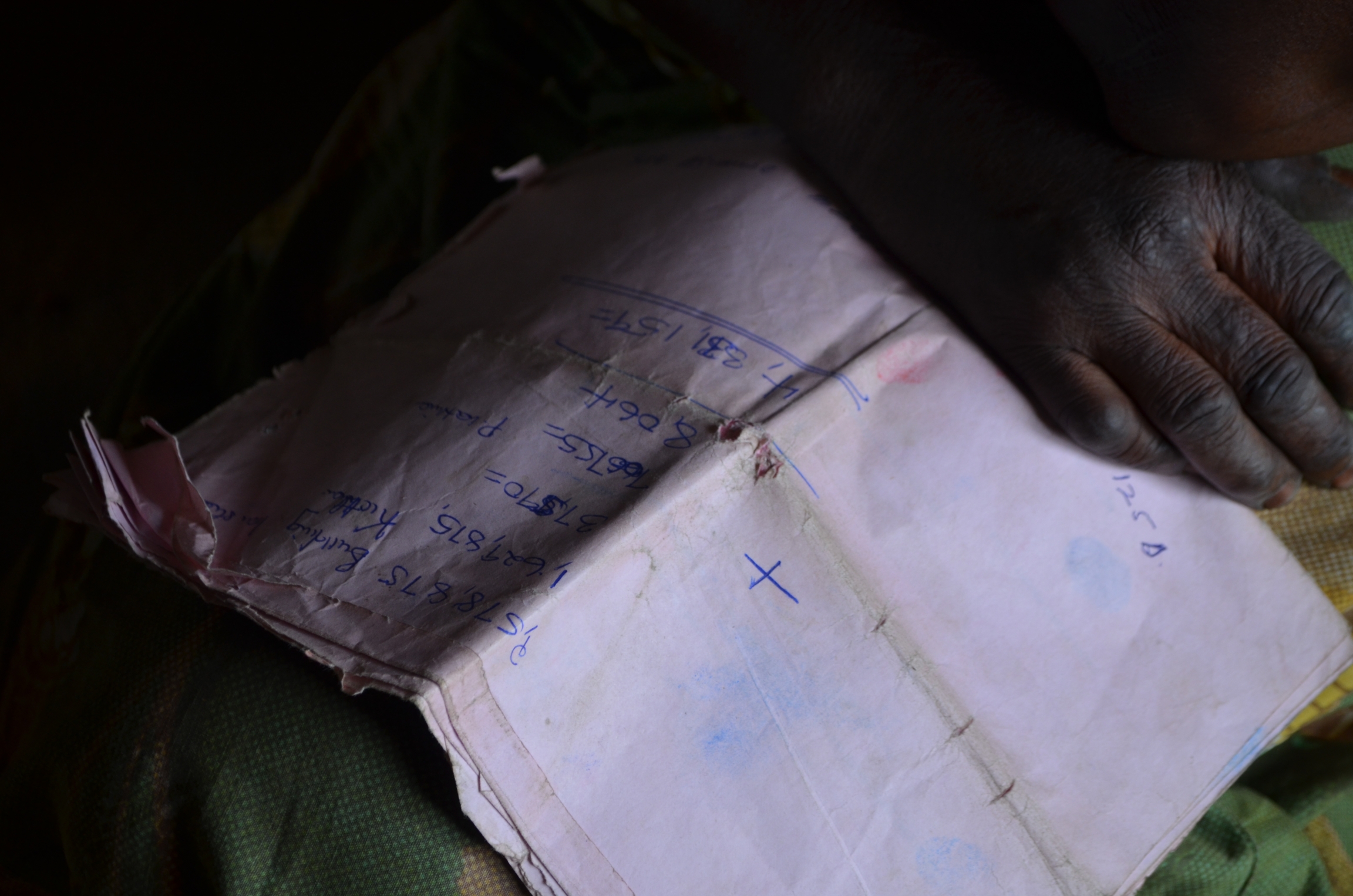 Margaret Asiimwe, one of the people forcibly relocated, holds a property evaluation written by Total's subcontractor, Atacama Consulting. She says her crops were undervalued. A hand holds a piece of paper with numbers written on it with pen ink