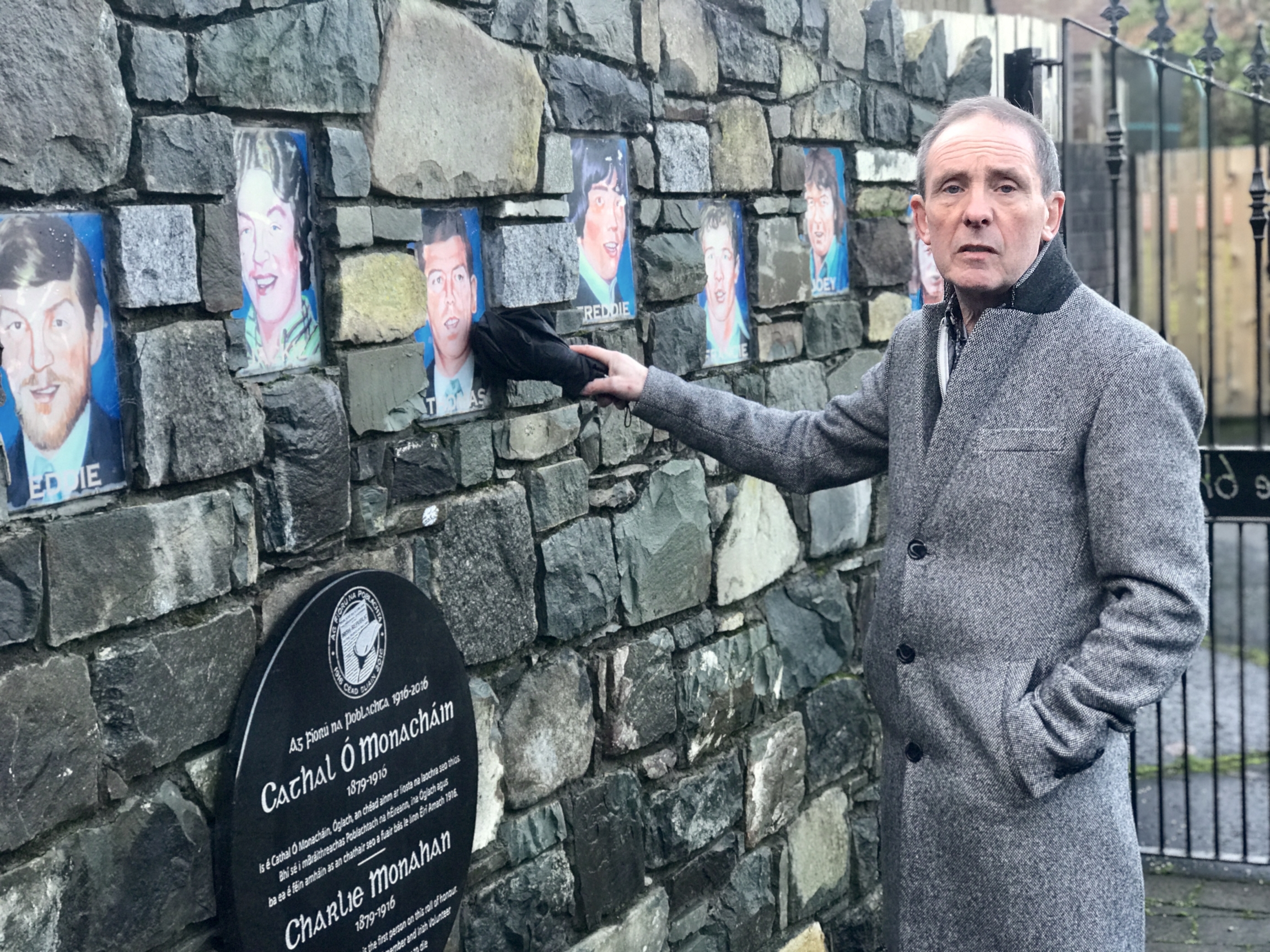 Un homme se tient devant un mur avec des portraits peints et en montre un.