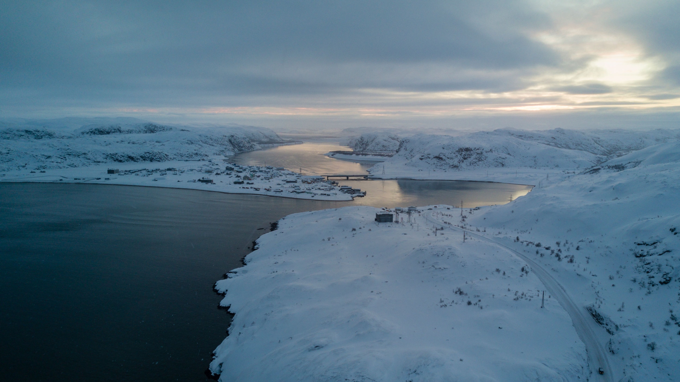 An aerial view of Teriberka village, the Teriberka river and the Barents Sea coast. An aerial view of Teriberka village showing a winding blue-colored river and the deep blue color of the Barents Sea coast.