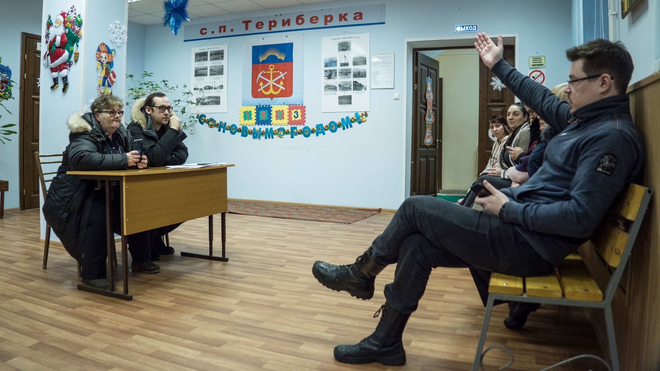 Elena Krivonos (L), at a meeting for the administration of Teriberka with the local people in the local House of Culture, Teriberka, Russia. A man and a woman are shown sitting at a small desk with a row of people across from them.